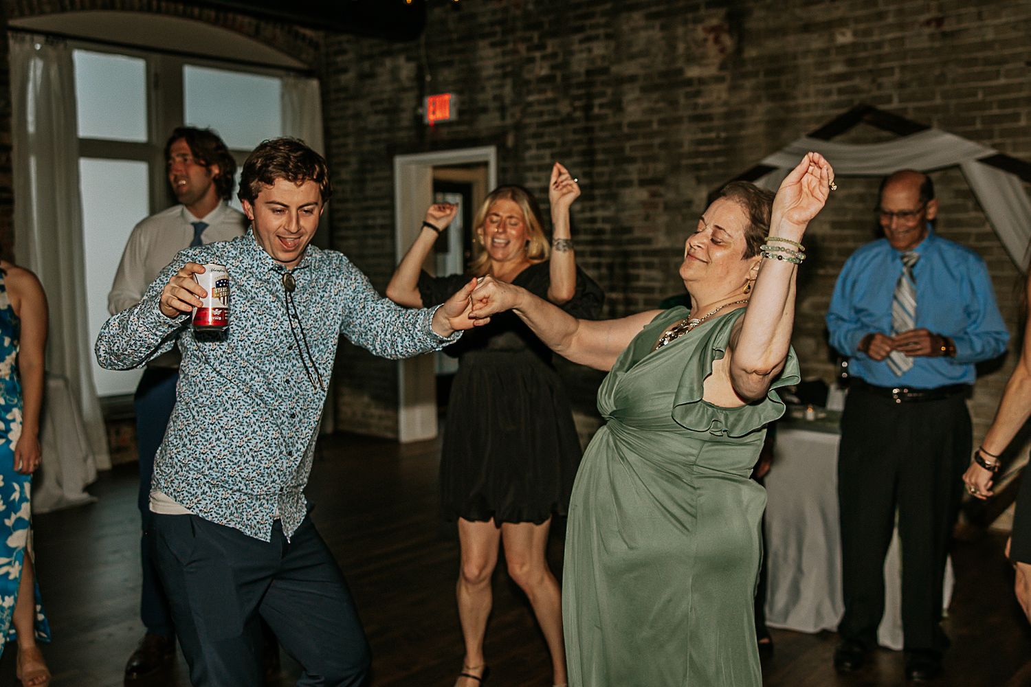 A man and woman in a green dress dance together at a lively wedding reception.