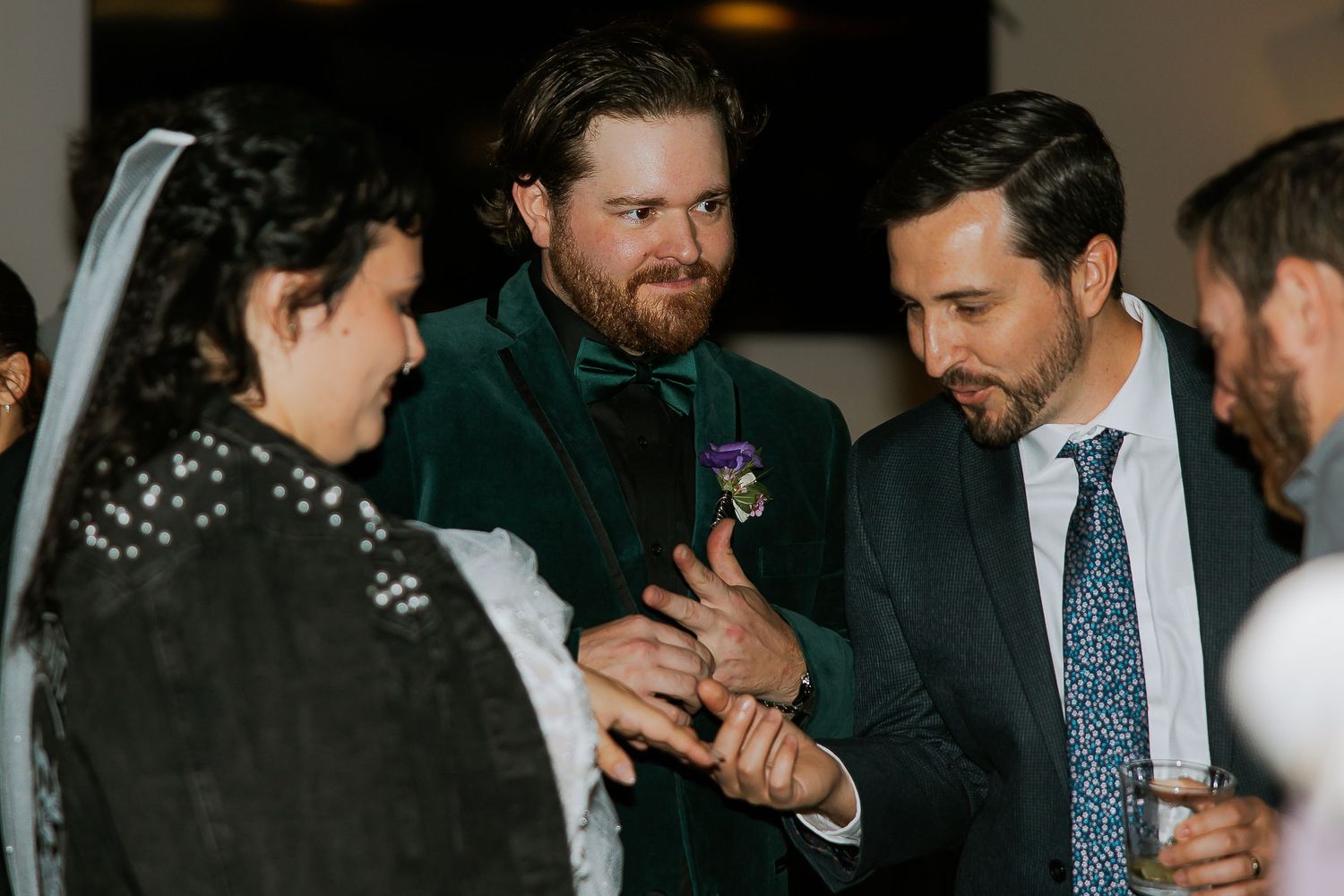 Groom in green velvet suit showing wedding ring to guests during cocktail hour celebration.