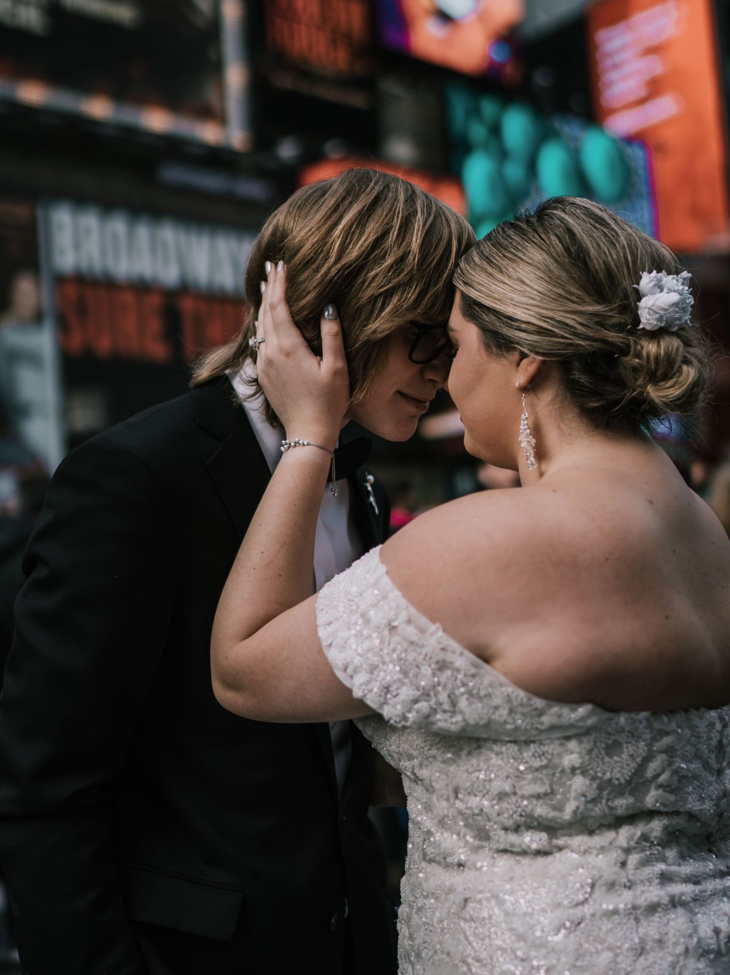 Intimate moment between bride and groom in Times Square NYC, bride in off-shoulder lace gown with floral hair piece.