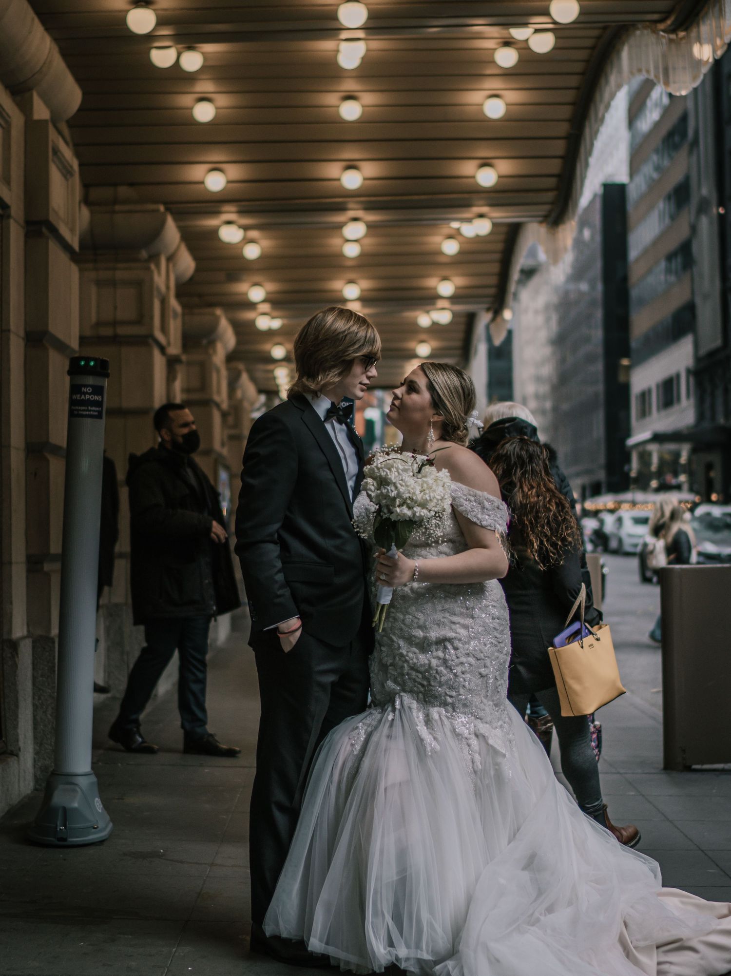 Bride and groom sharing a romantic moment under marquee lights outside a NYC theater holding white bouquet.