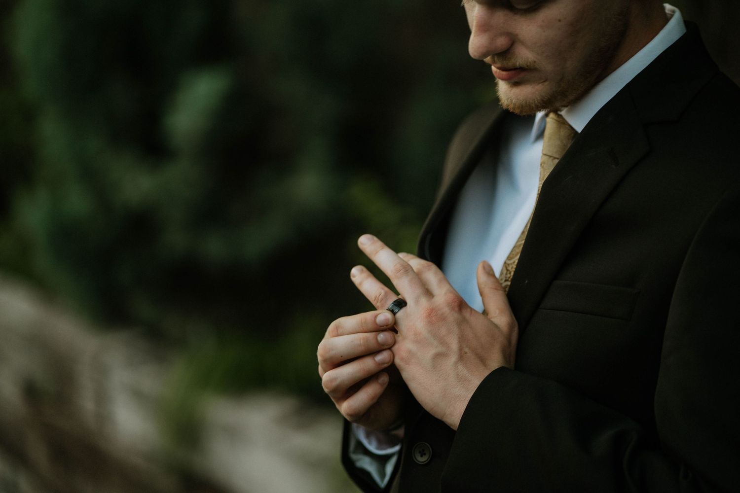 Groom in black suit with gold tie holding wedding ring close-up detail shot before ceremony at The Brightside in Dayton, Ohio