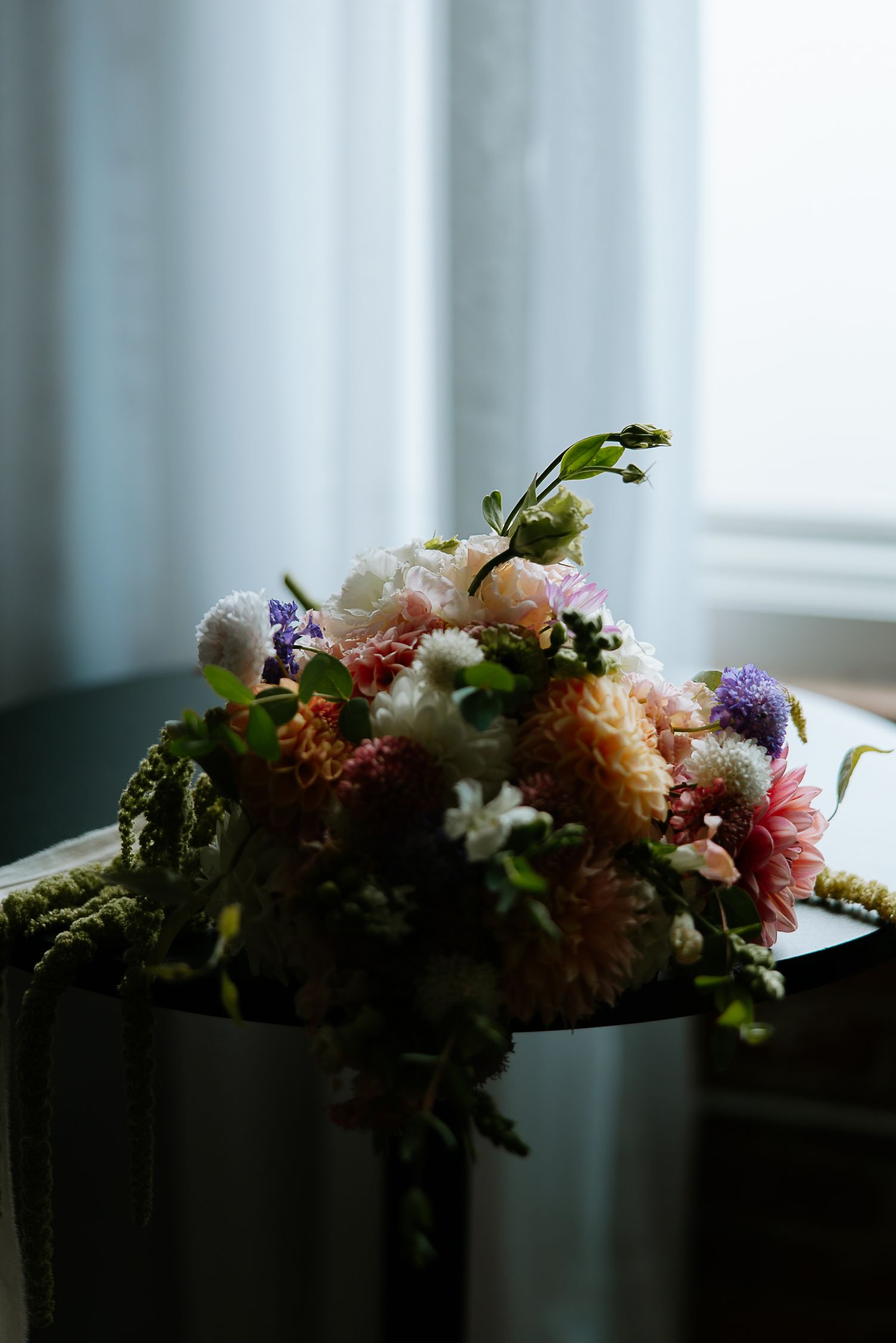Lush bridal bouquet with pink, white, and purple flowers resting on dark surface near a sunlit window at The Remedy in Dayton, Ohio