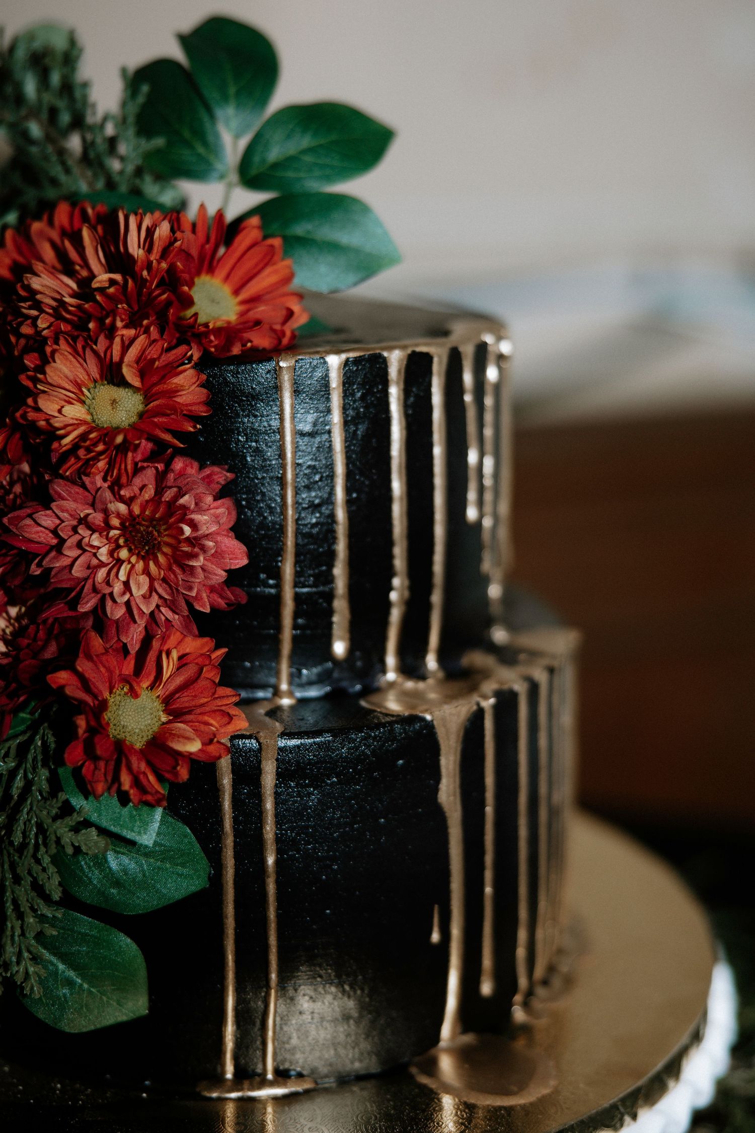 Two-tier black wedding cake decorated with gold drip detail and bold red floral arrangement at Urban Artifact in Cincinnati, Ohio