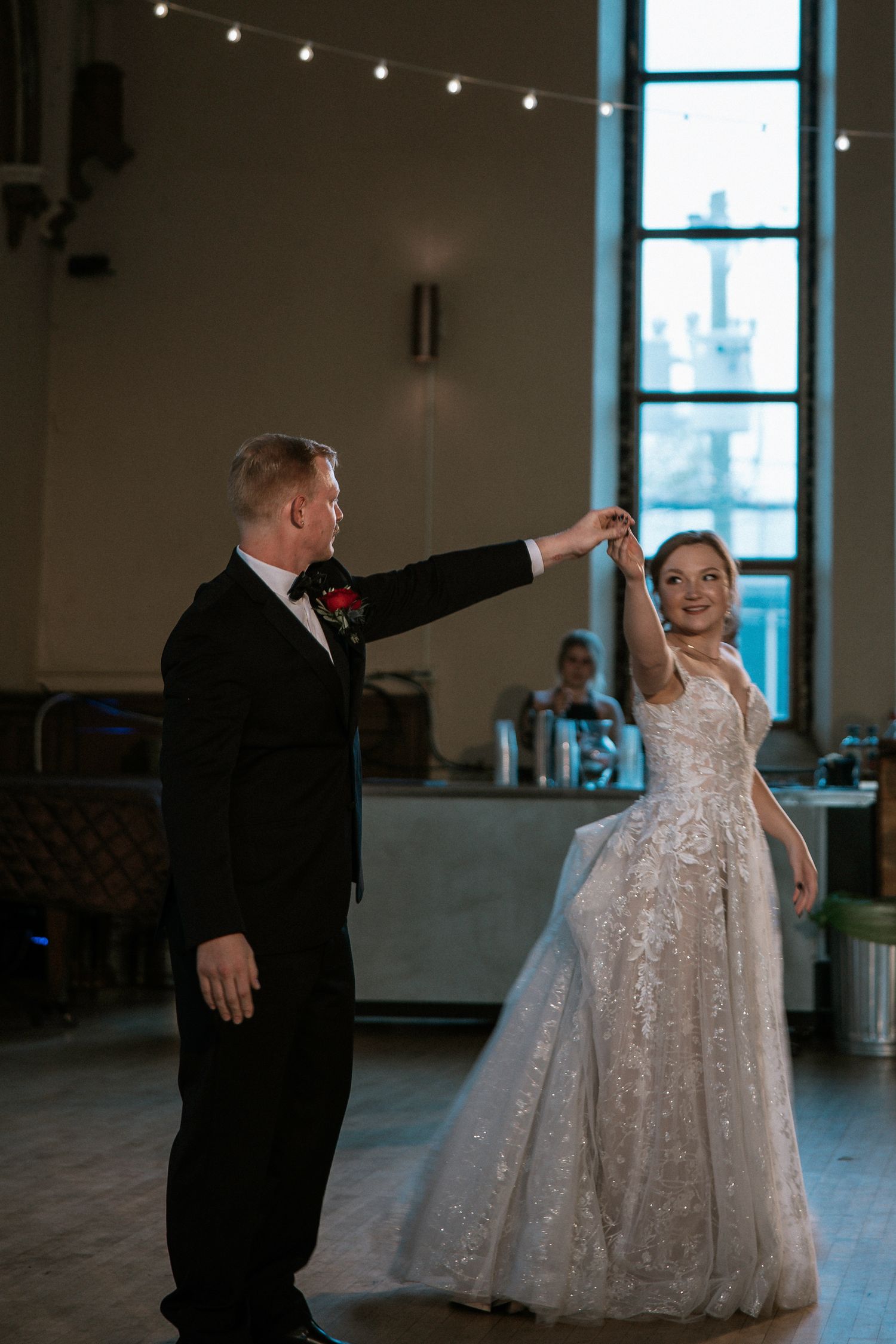 Bride in lace gown smiles as groom leads her in first dance in elegant reception hall at Urban Artifact in Cincinnati, Ohio
