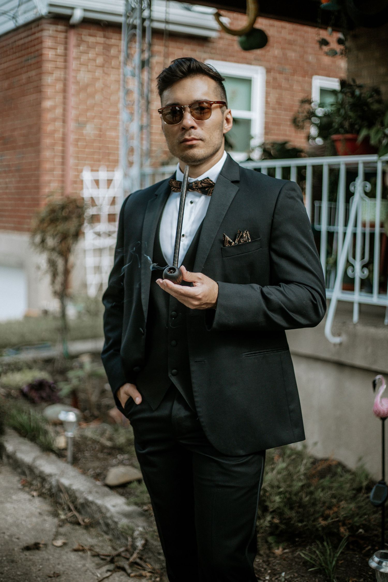 Stylish groomsman in black three-piece suit and sunglasses holds a pipe outdoors at a wedding in Cincinnati, Ohio