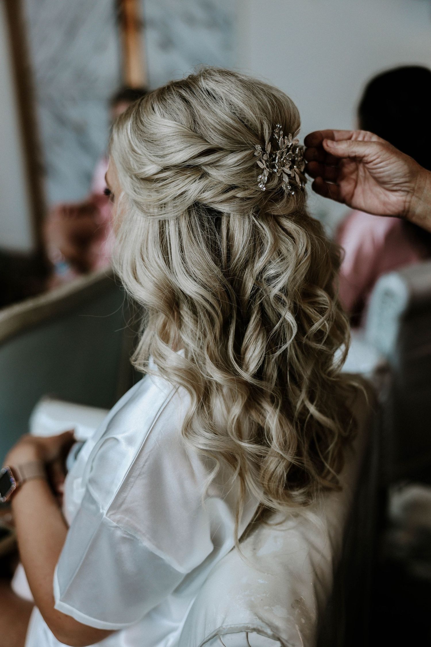 Blonde bride getting hair accessory placed in elegant half-up curled wedding hairstyle.
