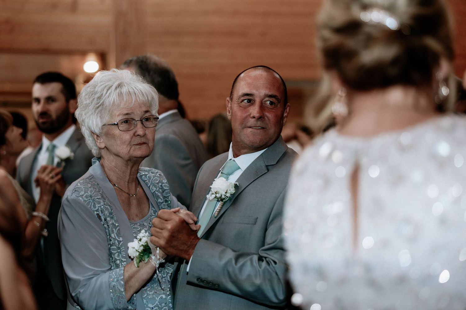 Elderly woman and man in gray suit watch emotional wedding ceremony in rustic barn venue.