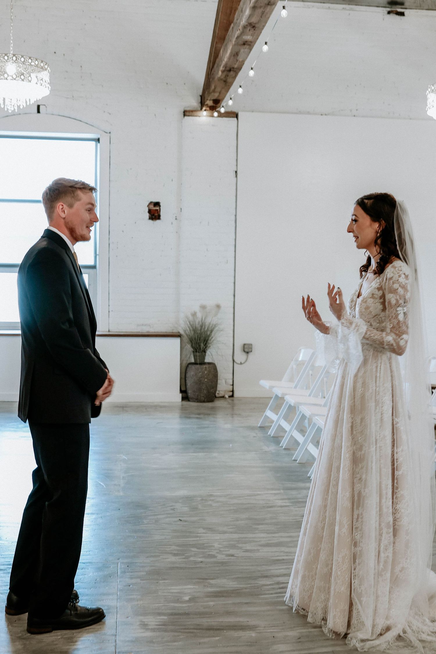 Bride in lace gown and groom share first look moment in bright white wedding venue.