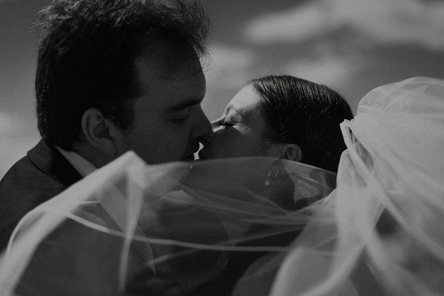 Black and white romantic photo of bride and groom kissing beneath flowing wedding veil.