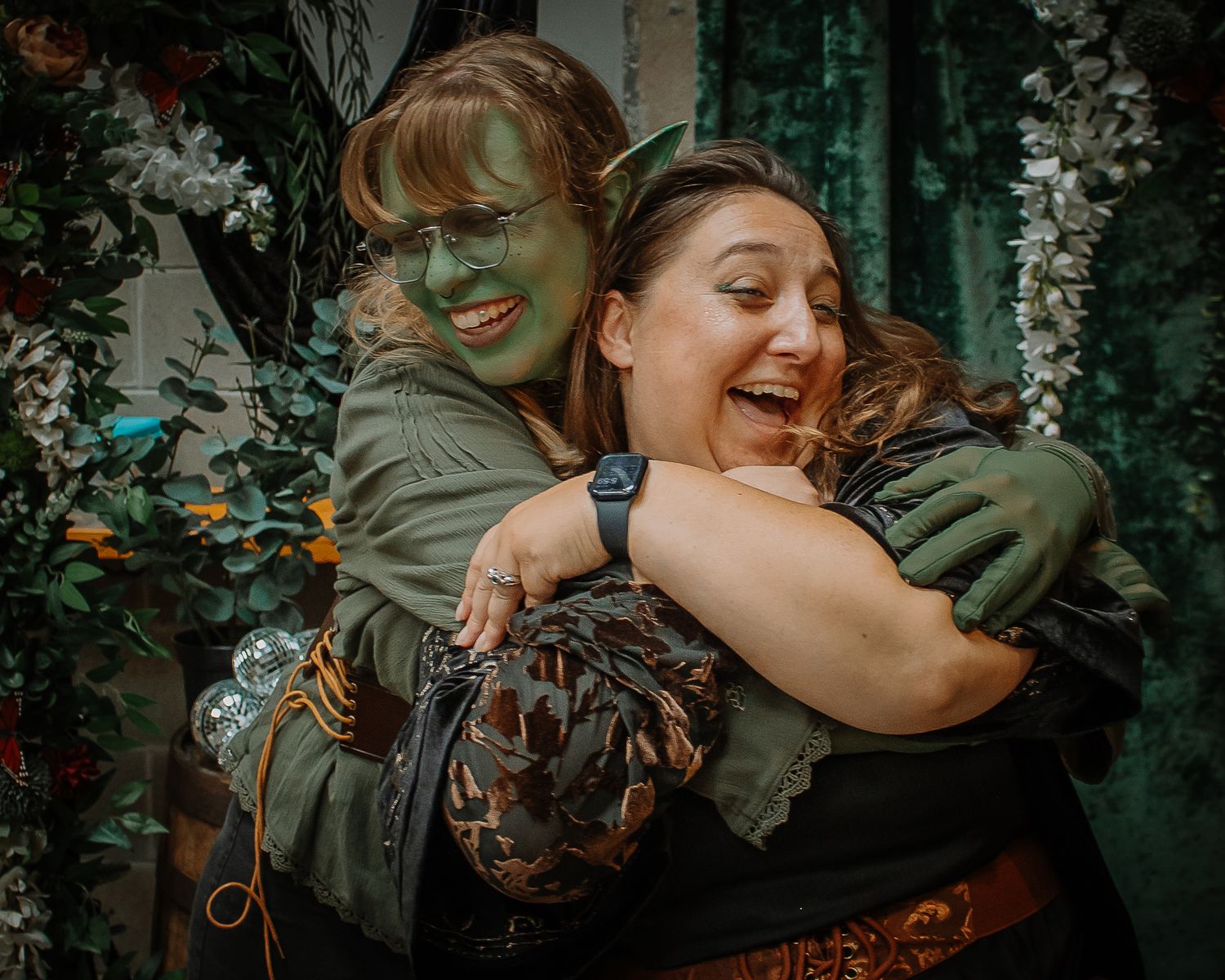 Two women hugging and laughing, one dressed in green Wicked Witch costume makeup and costume.