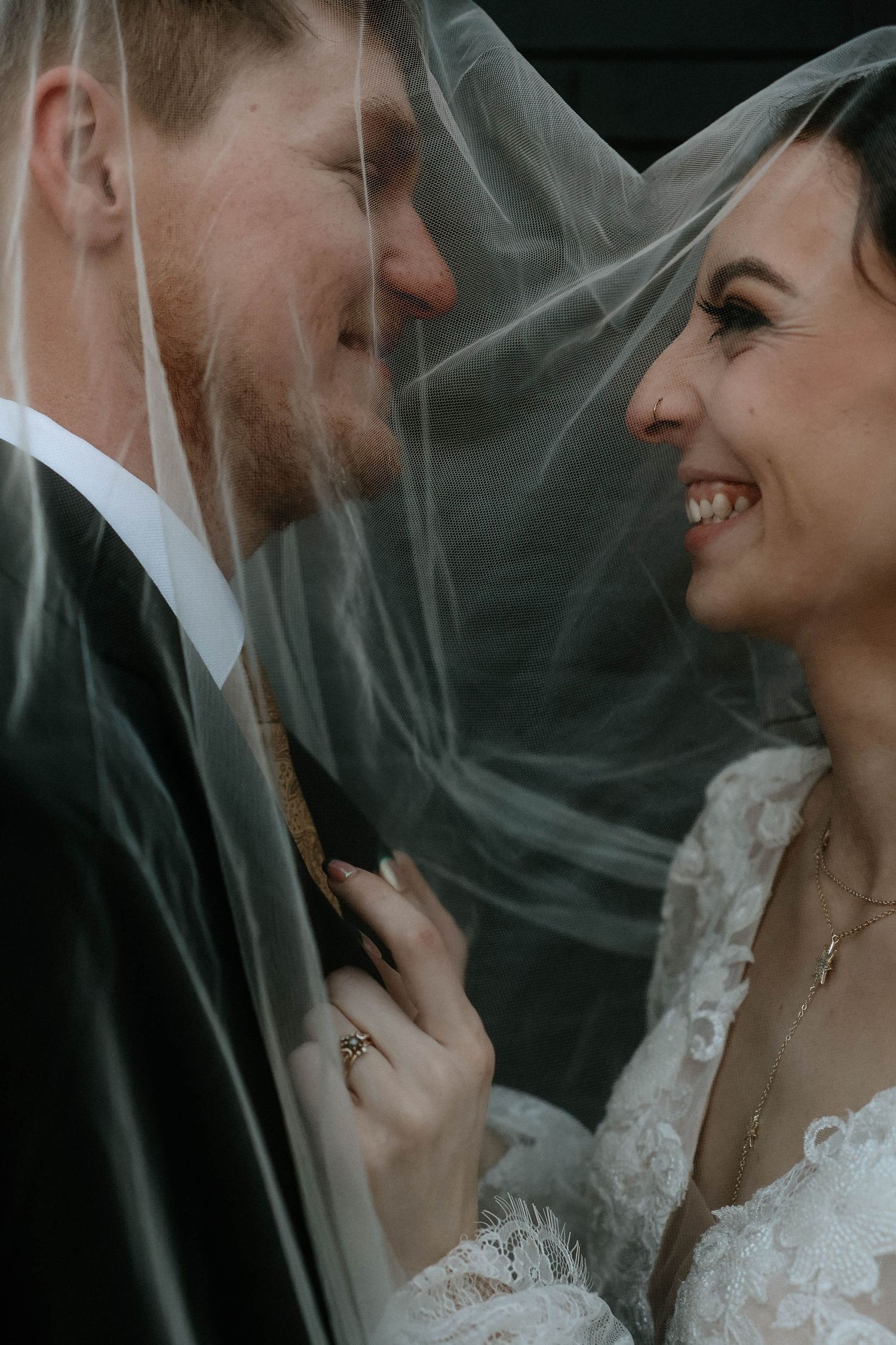 A bride and groom share a romantic moment under a flowing veil, smiling at each other on their wedding day.