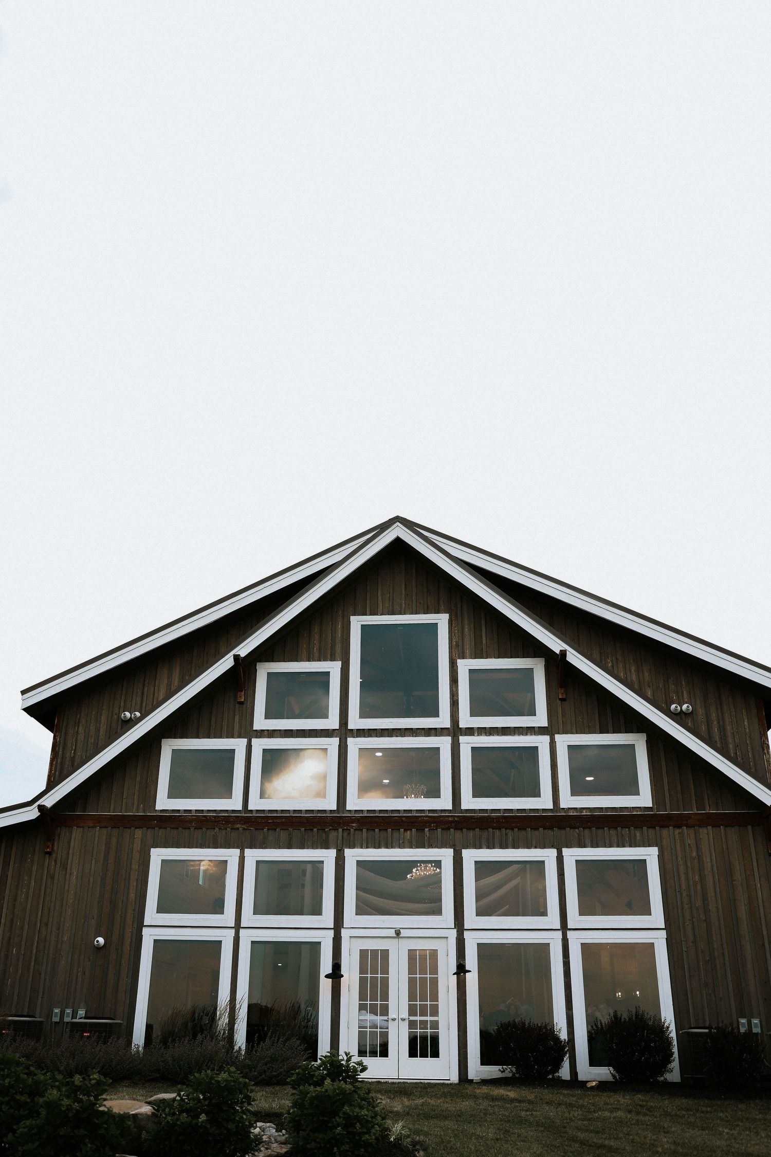 Rustic barn wedding venue with large white-framed windows and wood siding under an overcast sky.