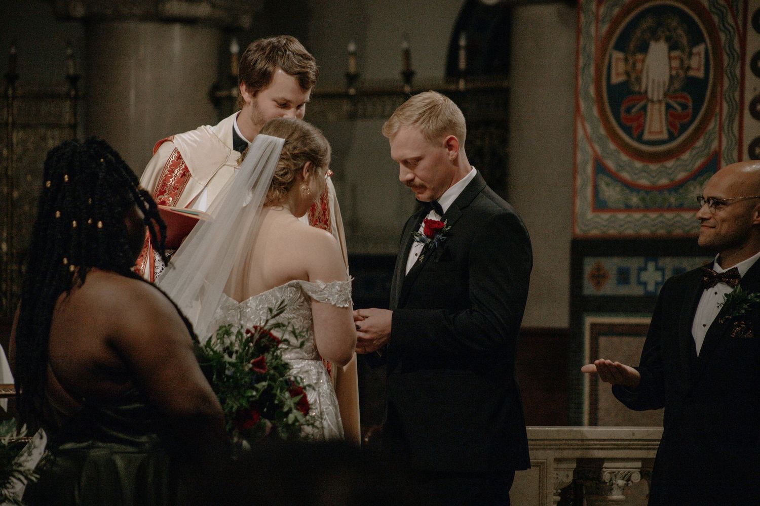 Groom places ring on brides finger as priest and witnesses observe at church altar in Cincinnati, Ohio