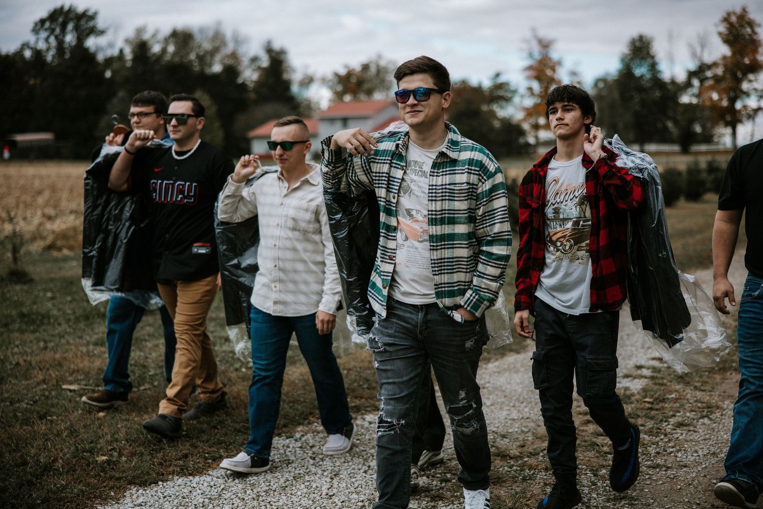 Group of young men in casual attire walking confidently down a rural dirt path wearing sunglasses on a fall day.