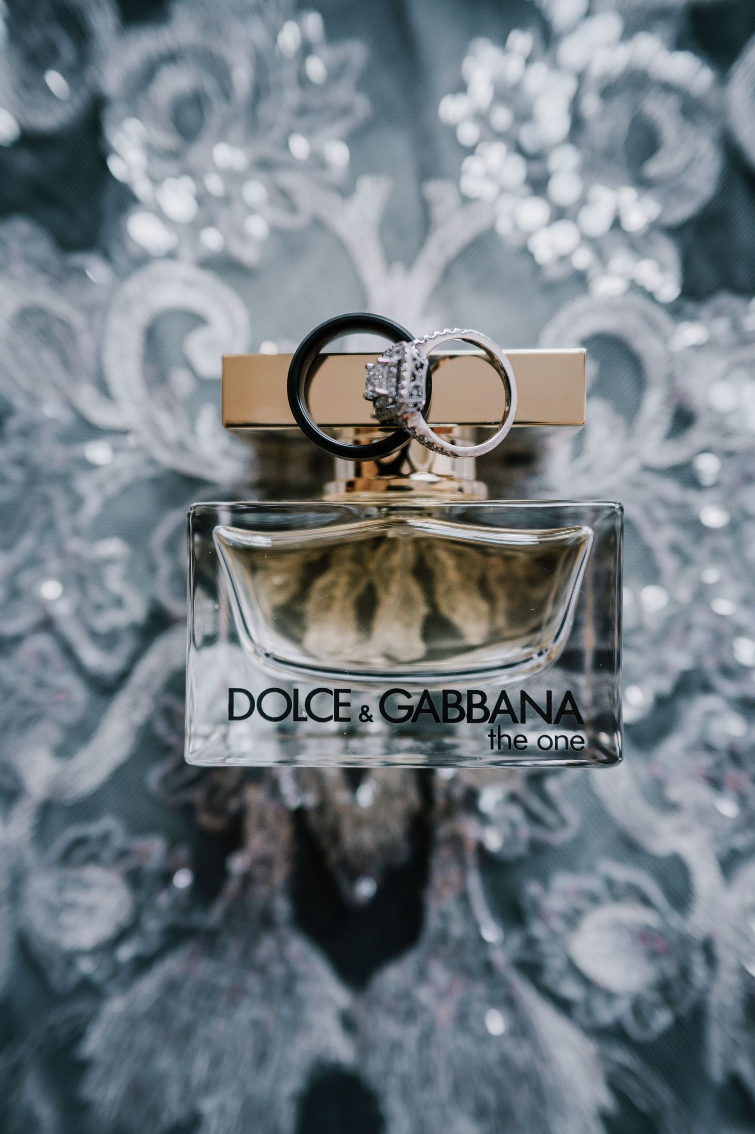 Dolce and Gabbana The One perfume bottle with wedding rings on lace fabric.