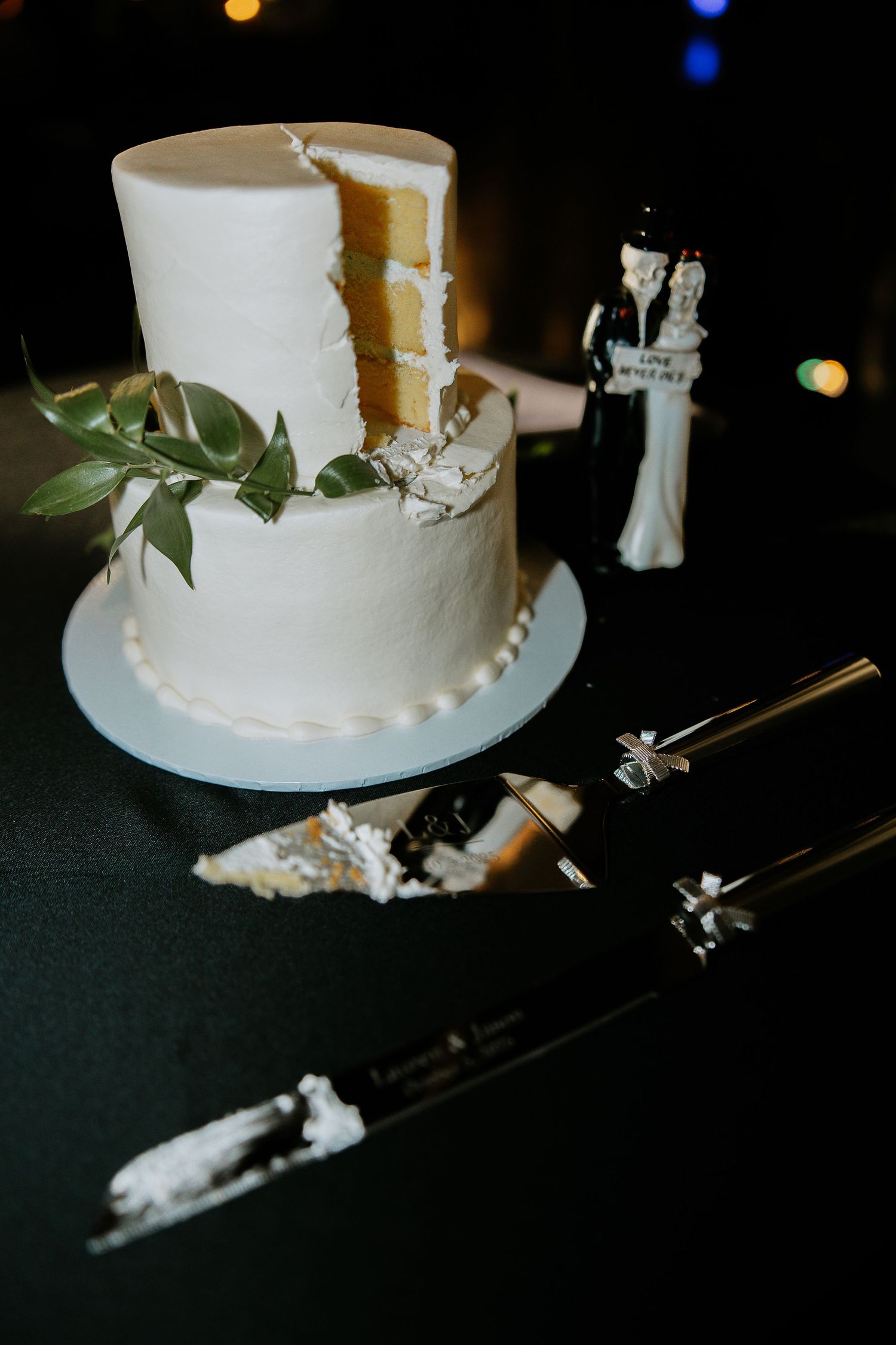 Two-tier white wedding cake with greenery and classic bride and groom topper on table.
