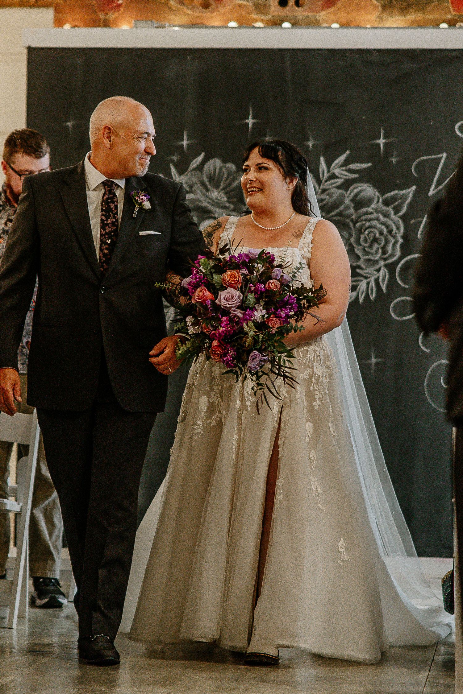 Bride and father share a joyful glance while walking down the aisle together.