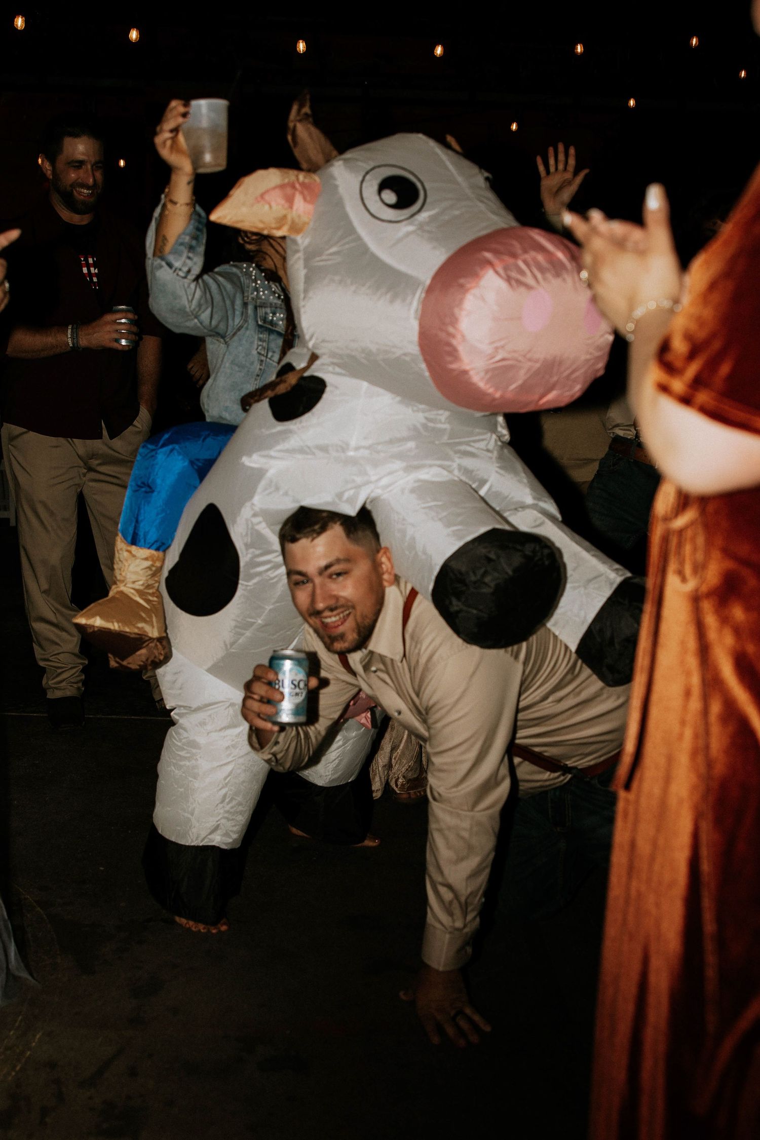 Groom in inflatable cow costume crouching and holding beer can during lively outdoor reception party at The Brightside in Dayton, Ohio