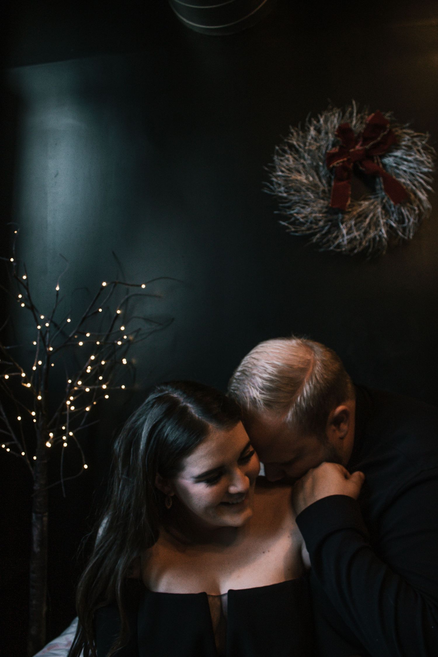 Romantic couple sharing an intimate moment near a glowing twig tree and festive wreath decor at Millstreet Studios in Cincinnati, Ohio.