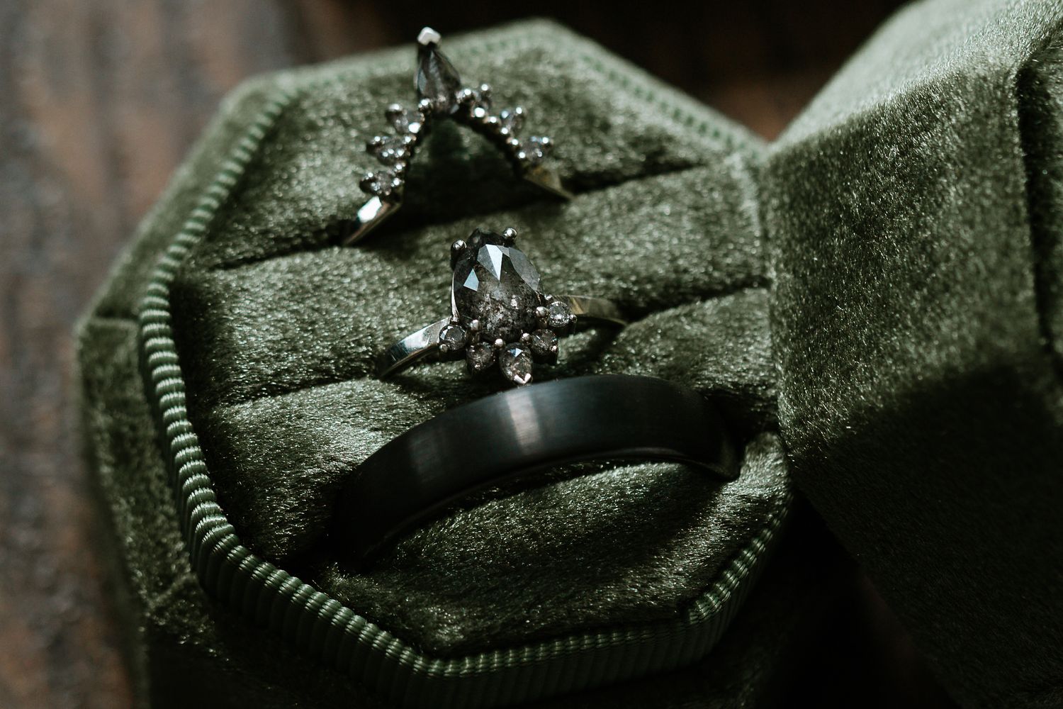 Close-up of diamond engagement ring and black wedding band in a green velvet octagonal ring box.