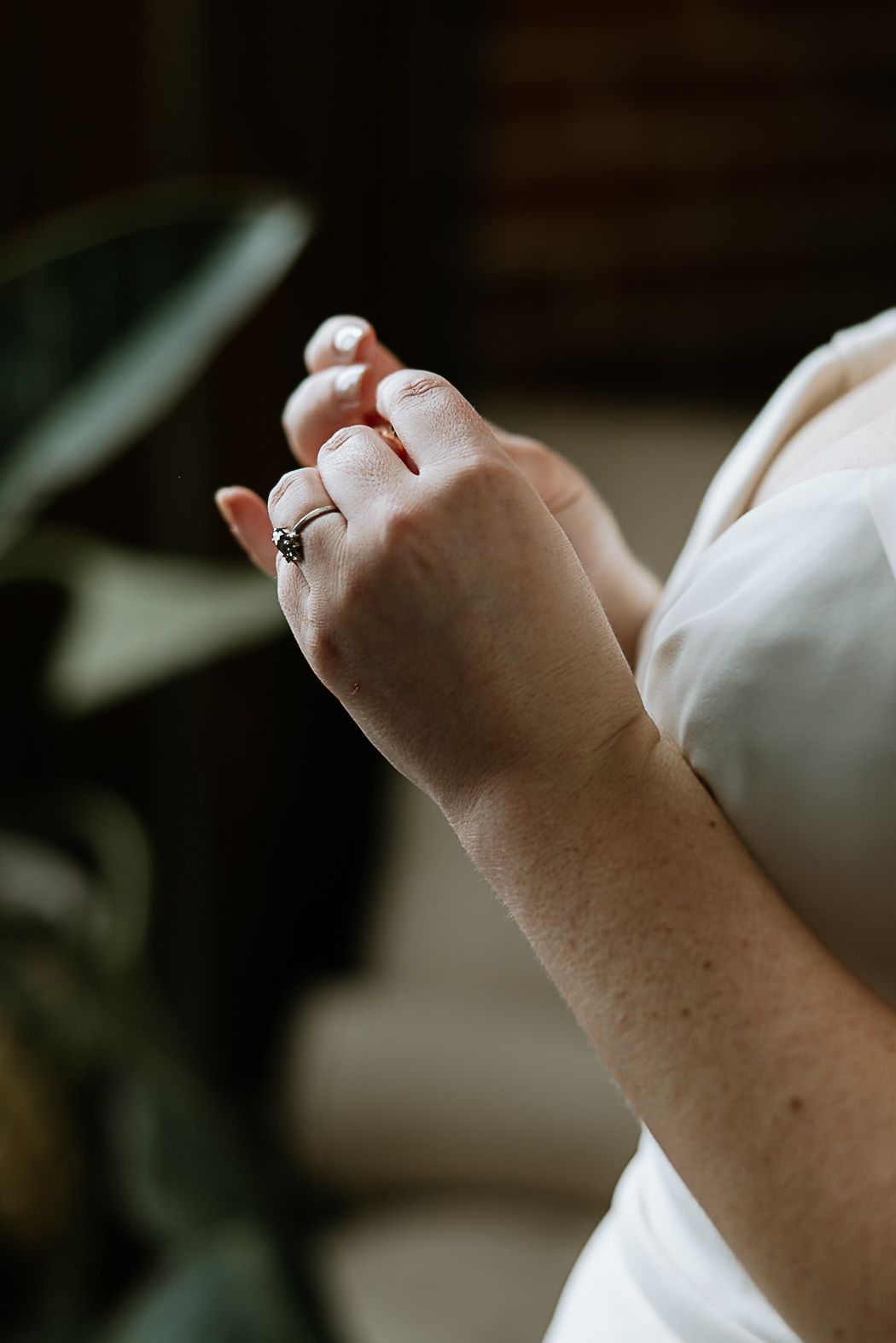 Close-up of bride's hands wearing an engagement ring in a white wedding gown.
