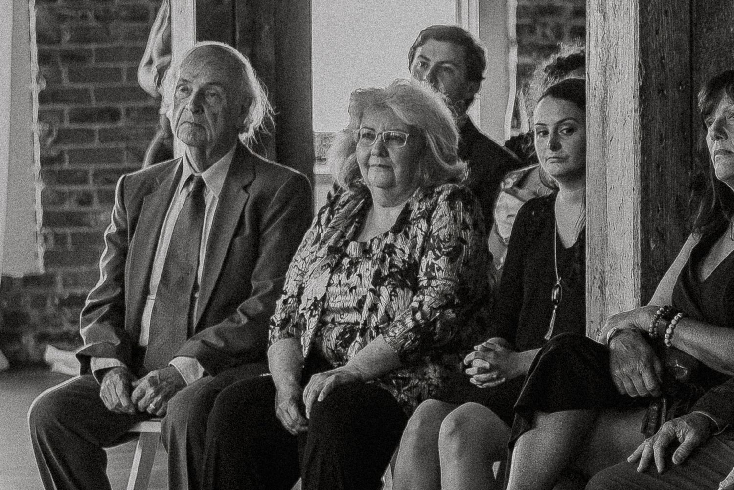 Guests seated at an indoor wedding ceremony, captured in black and white photography.