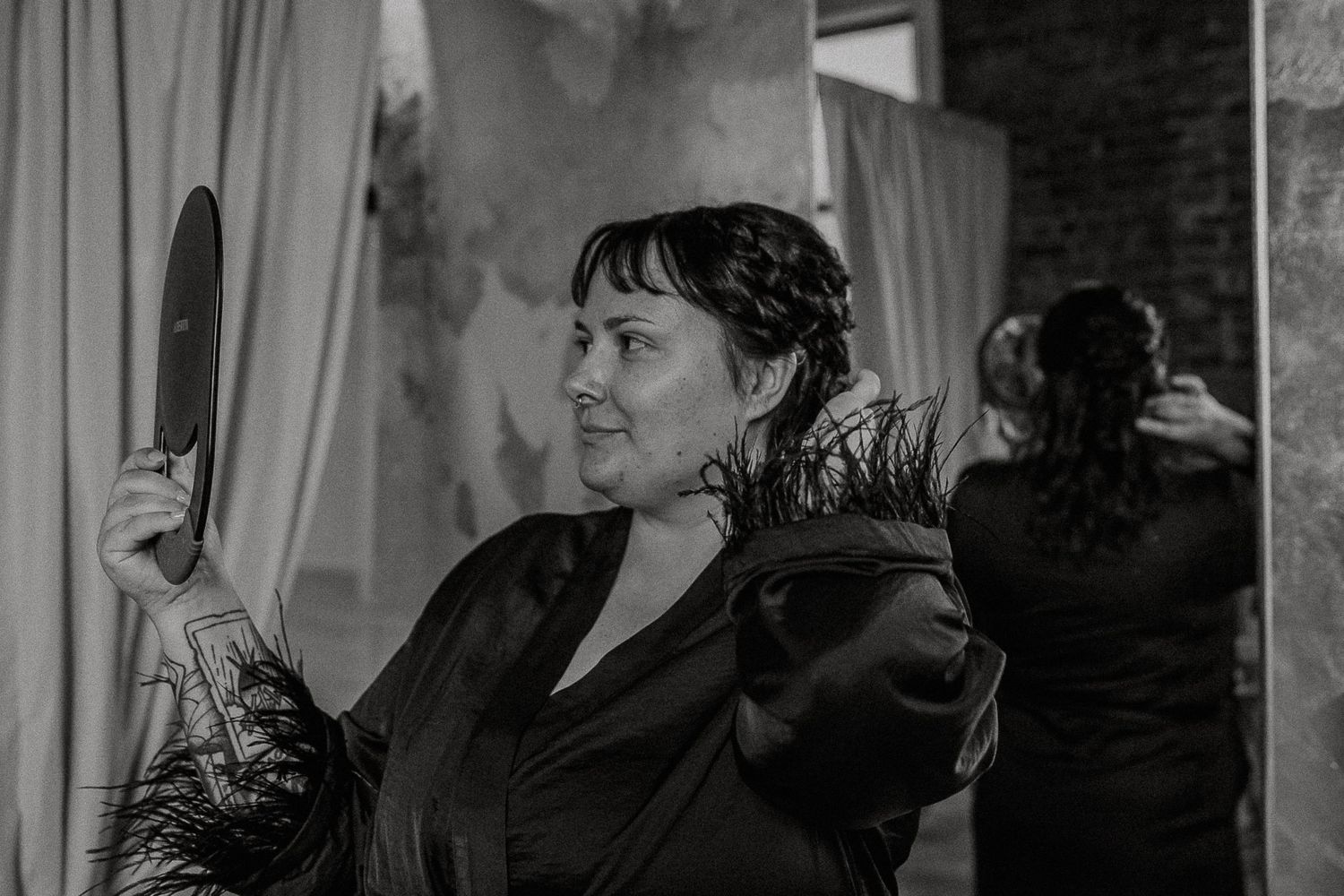 Black and white photo of a woman holding a mirror and feathers at an indoor event.