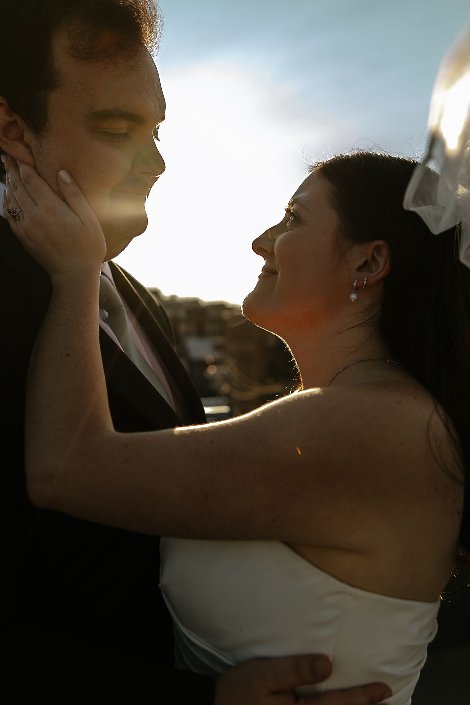 Bride tenderly holding grooms face in golden sunset light at wedding.