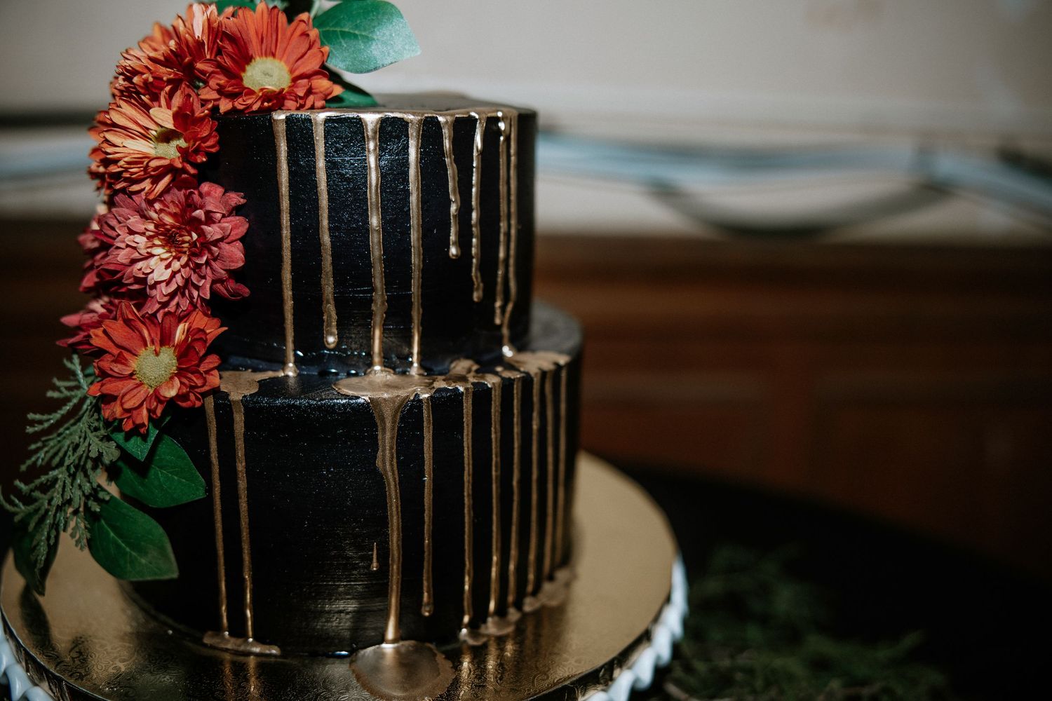 Black two-tier wedding cake with gold drip accents and red flower decorations on gold stand at Urban Artifact in Cincinnati, Ohio
