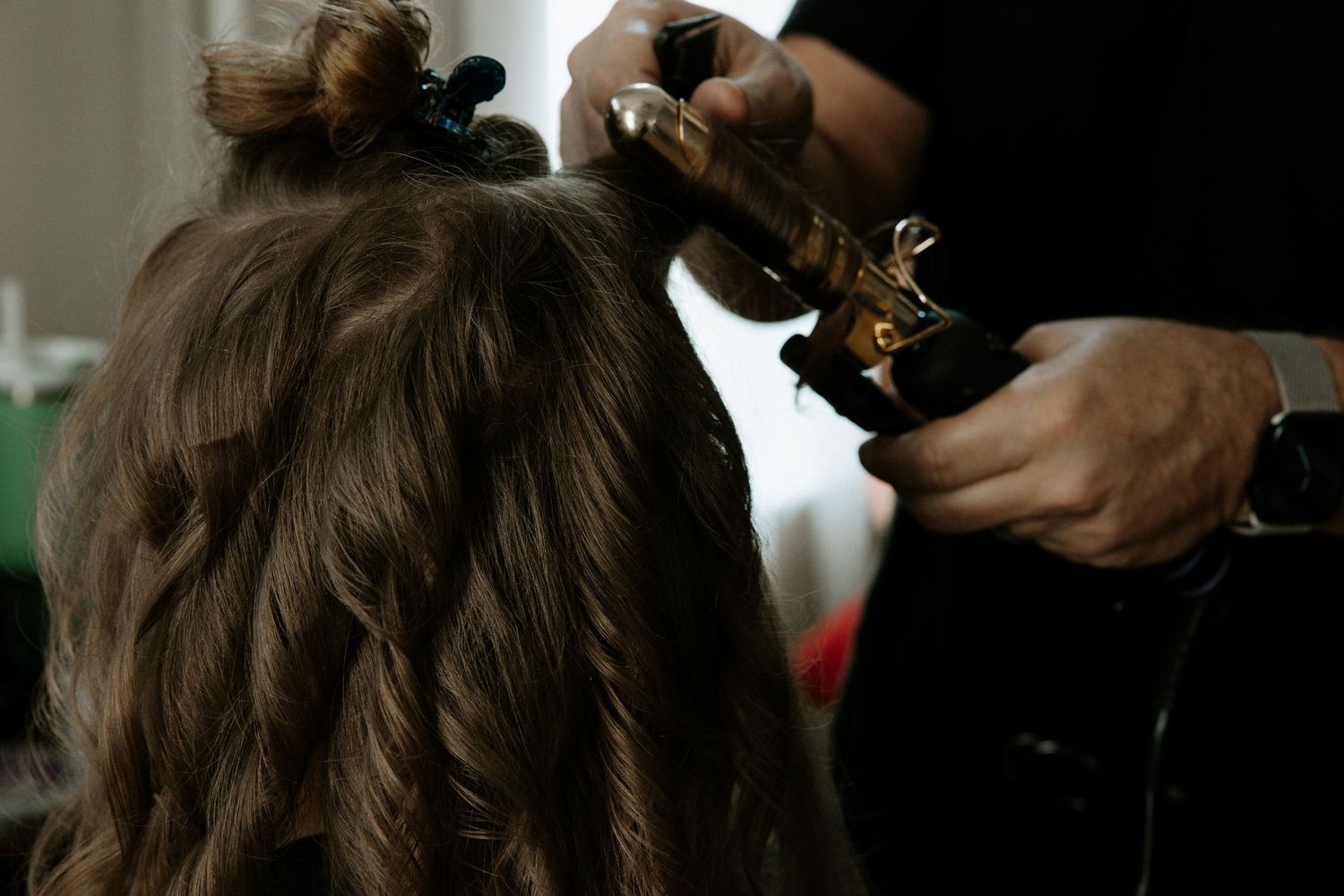 A hairstylist curling long brown hair with a gold curling iron during a bridal preparation session at Urban Artifact in Cincinnati, Ohio