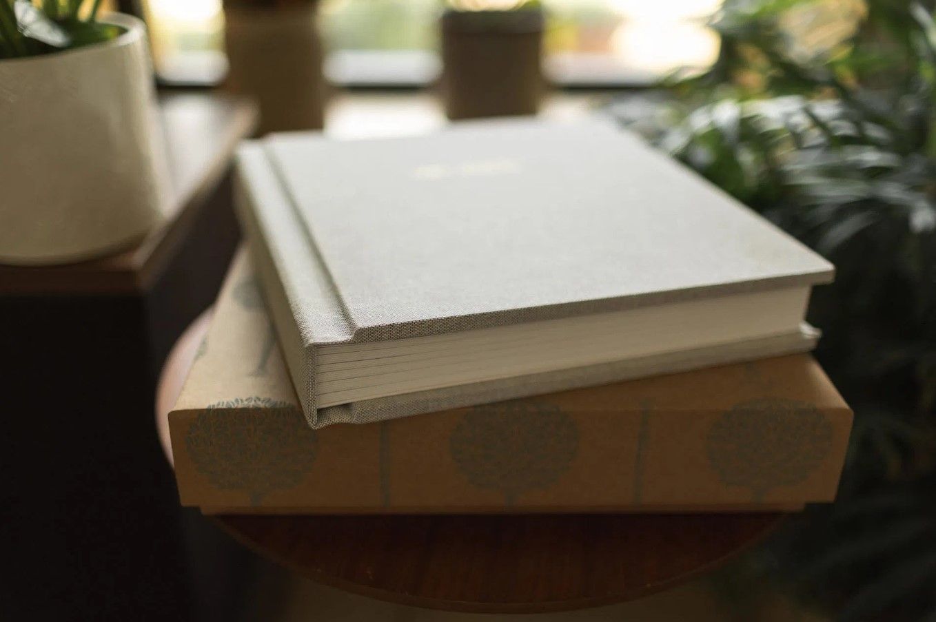 Two stacked hardcover photo books with white linen covers on a round wooden table in Cincinnati, Ohio