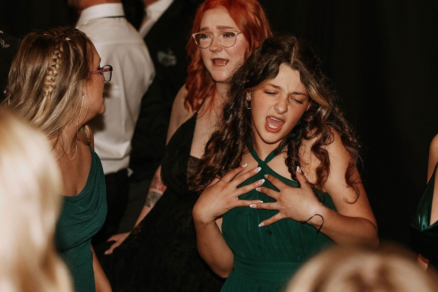Women in green dresses dancing energetically at a formal event or wedding reception.