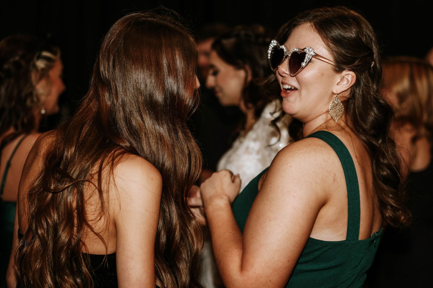 Two women in elegant dresses dancing and laughing together at a formal evening event or wedding reception.