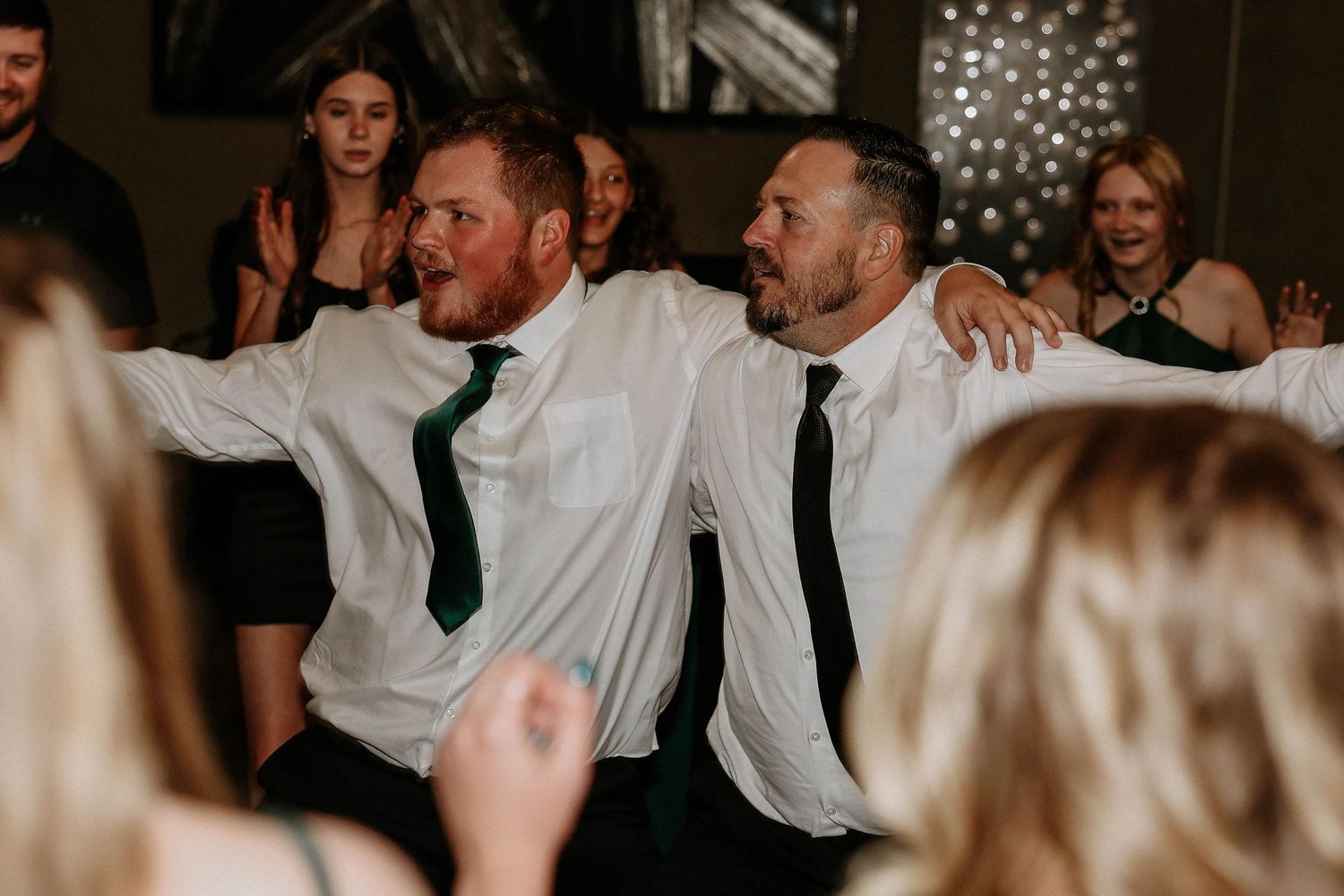 Two men in white shirts and ties dancing together at a wedding reception party.