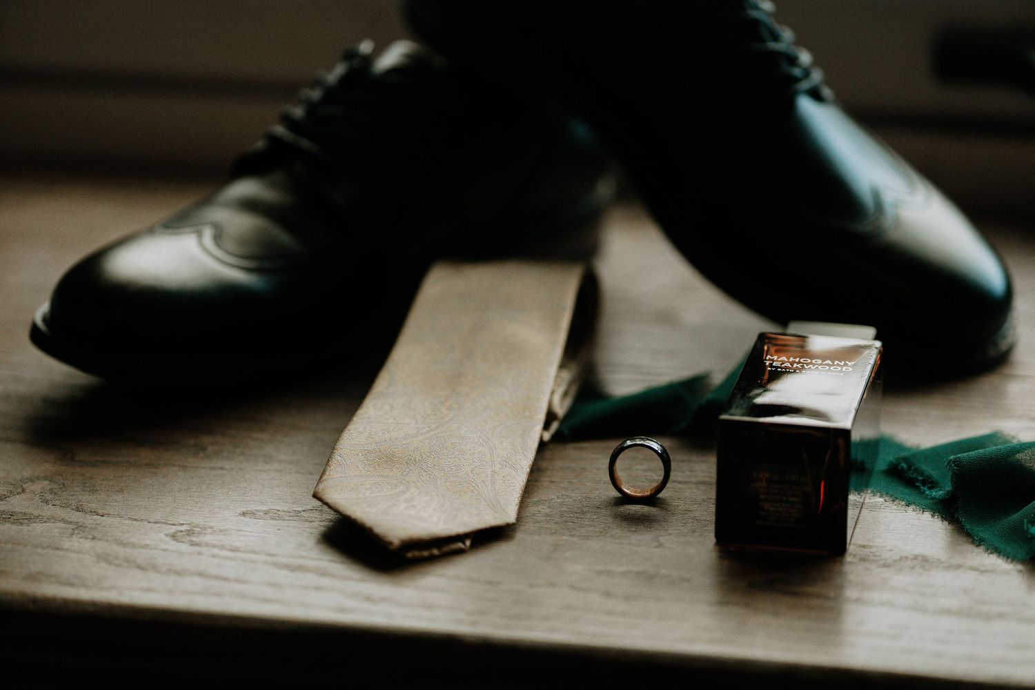 Groom wedding accessories flat lay featuring tan tie, black dress shoes, ring, and cufflinks on wood at The Brightside in Dayton, Ohio
