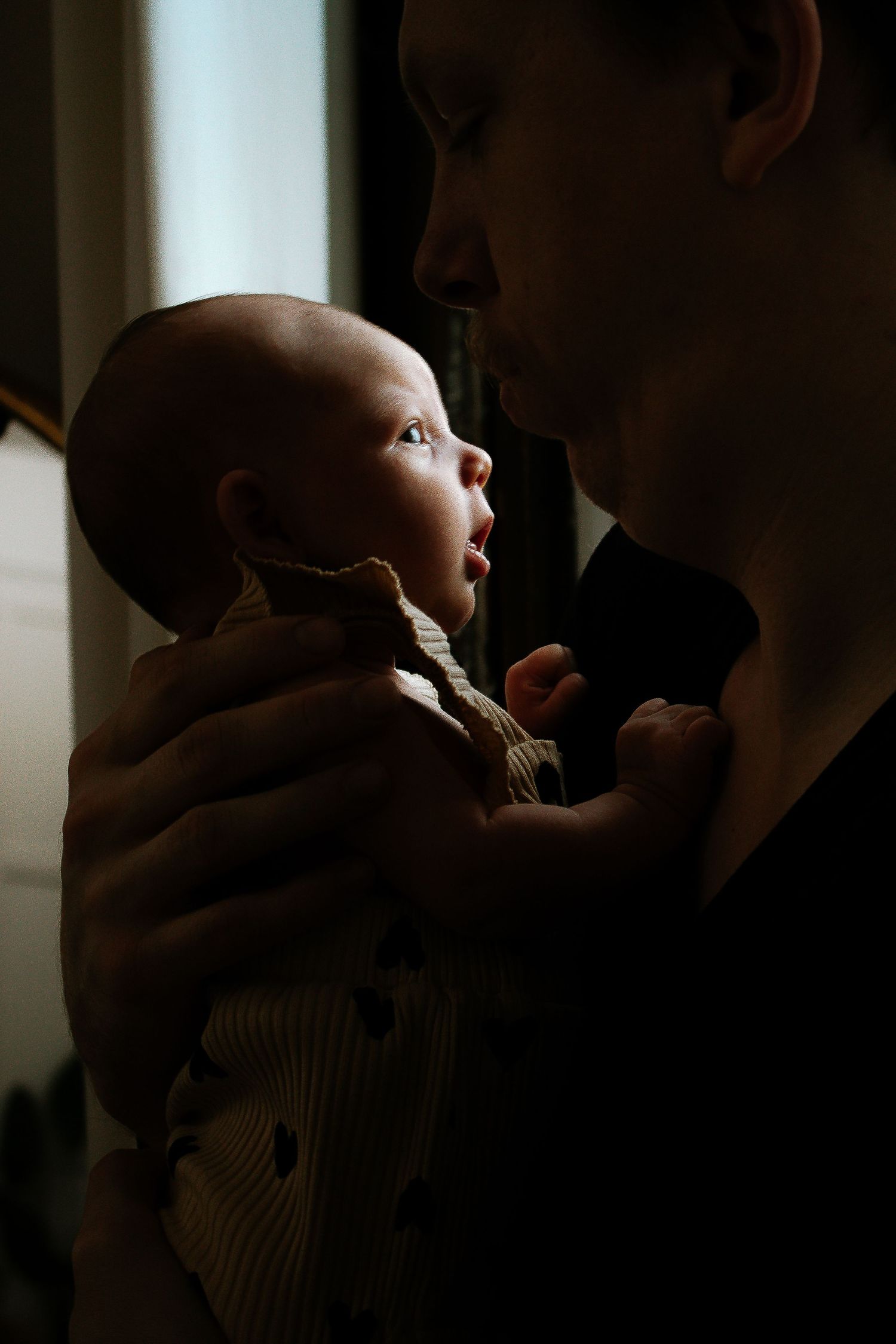 Father holding alert newborn baby in dim natural light in Cincinnati, Ohio.