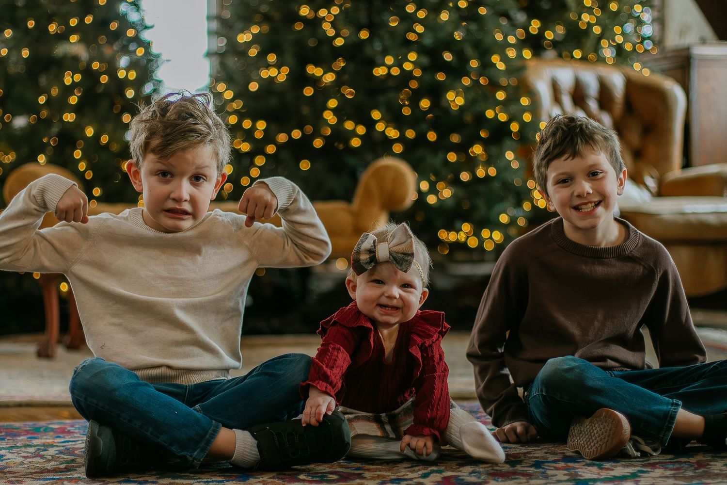Three siblings sitting together in front of a decorated Christmas tree, smiling at Mill Street Studios in Cincinnati, Ohio.
