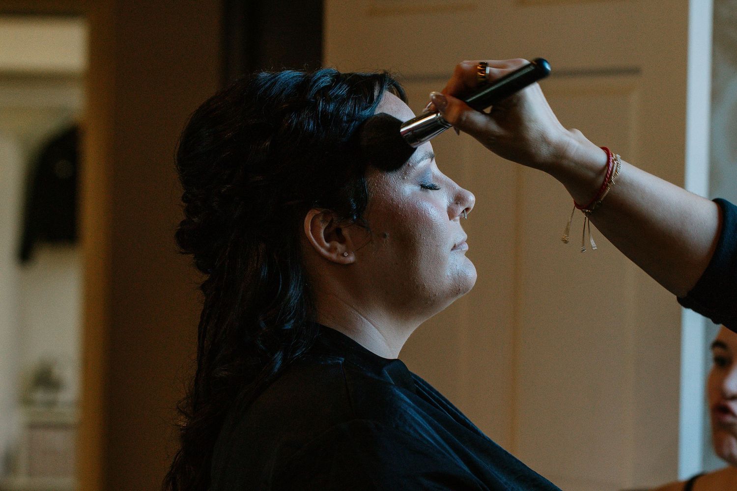 Hair stylist using curling iron on bride with dark hair during wedding prep.