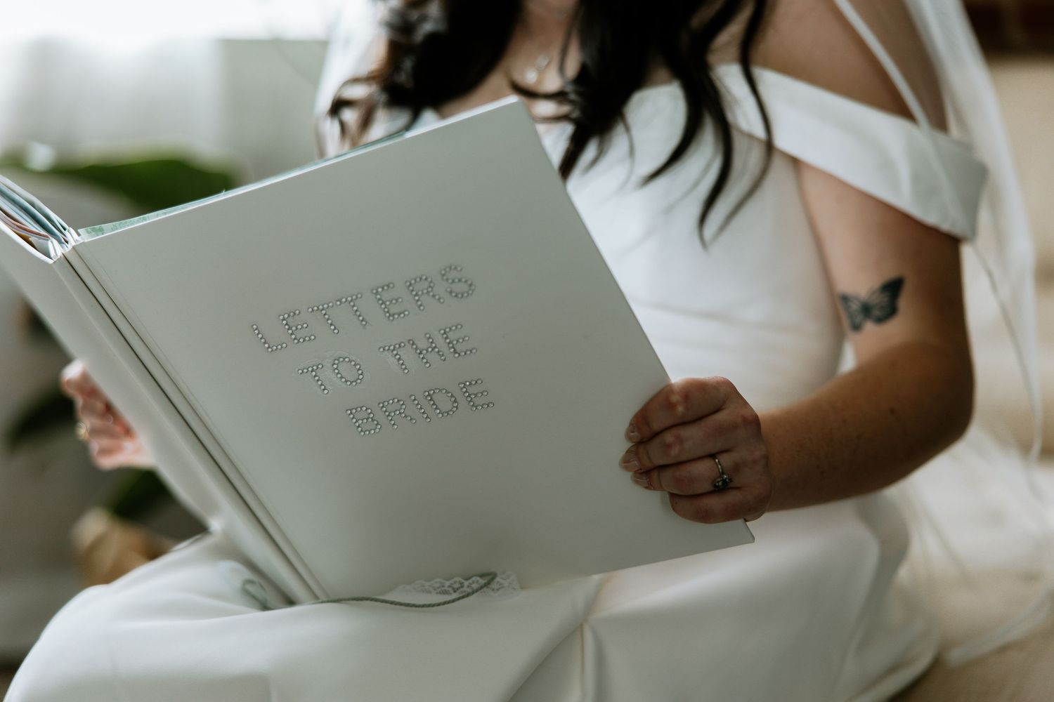 Bride in white off-shoulder gown reading a Letters to the Bride keepsake book.
