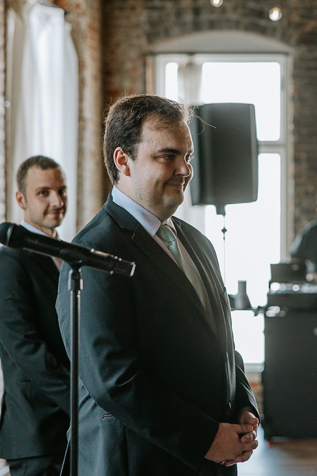 Groom in dark suit with green tie standing at altar smiling during wedding ceremony.