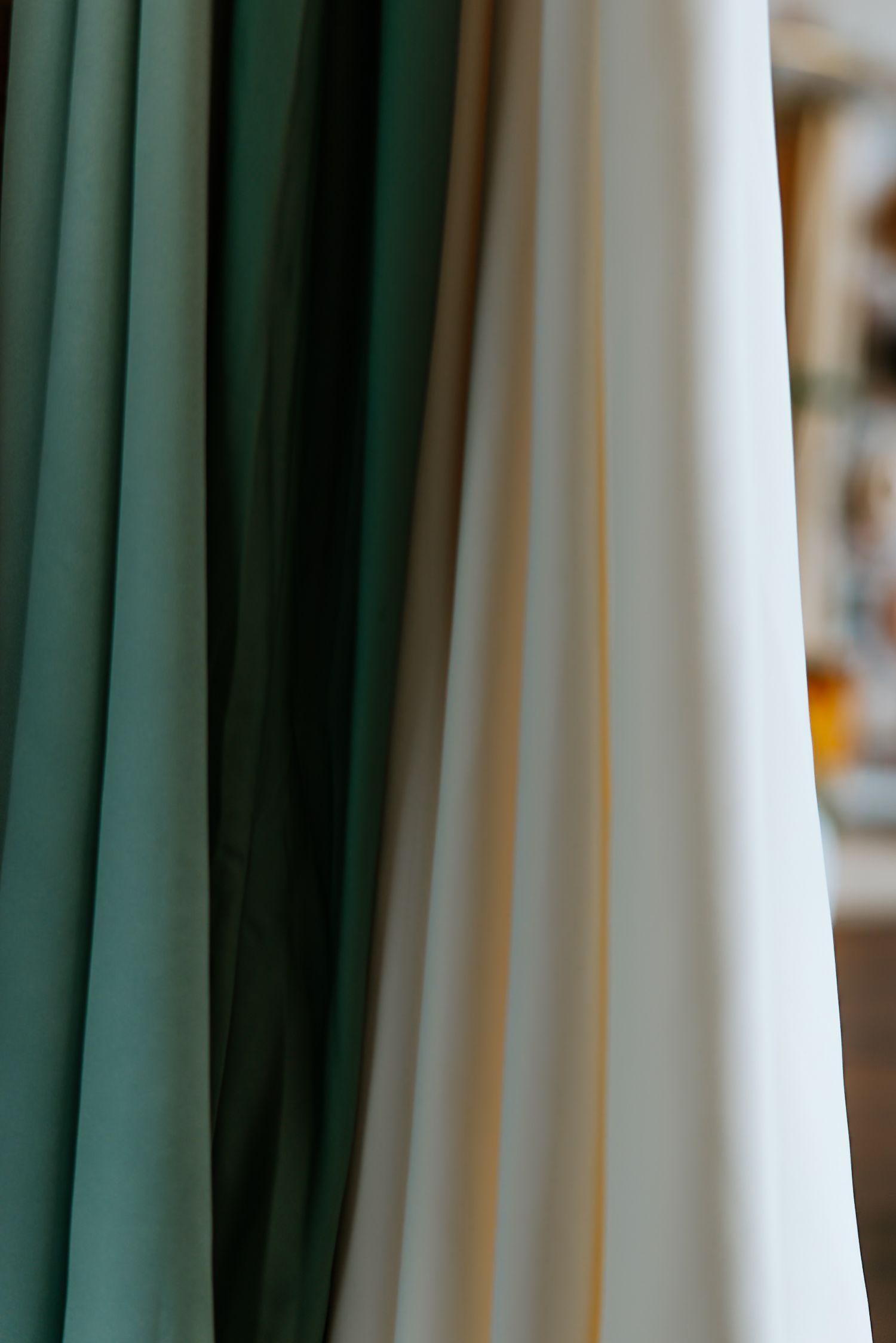 Green bridesmaid dress and white wedding gown hanging side by side with soft bokeh background.