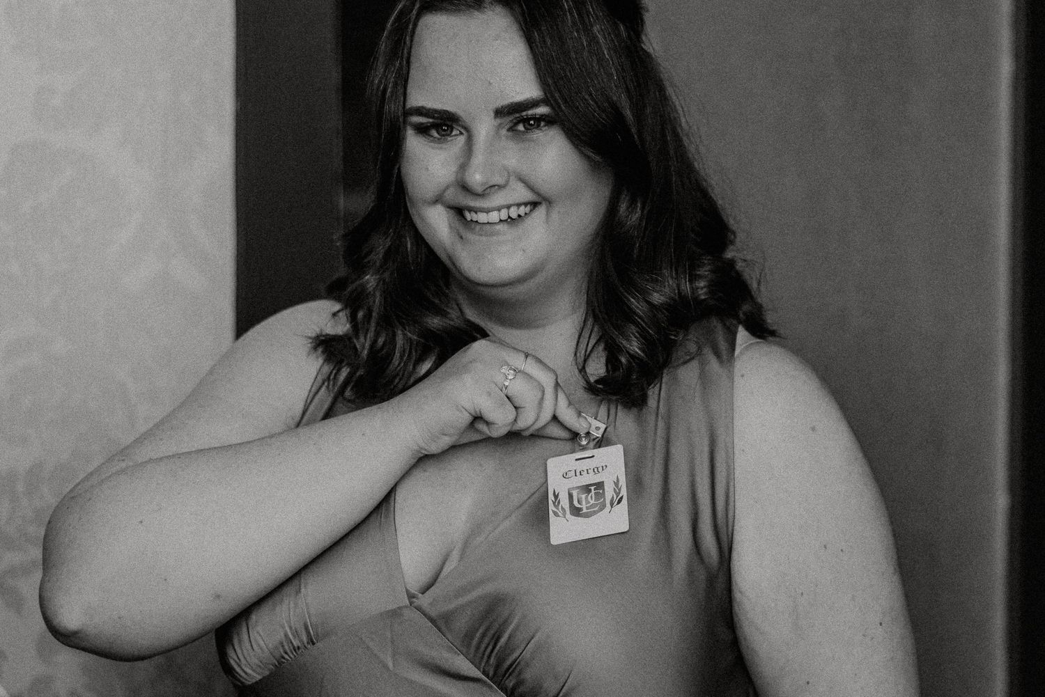 Black and white photo of smiling bridesmaid in satin dress holding a name tag at a wedding.