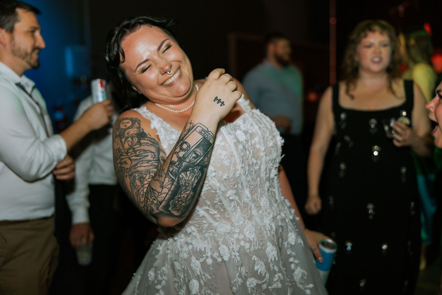 Bride in lace wedding gown laughing and dancing under blue lights at her reception.