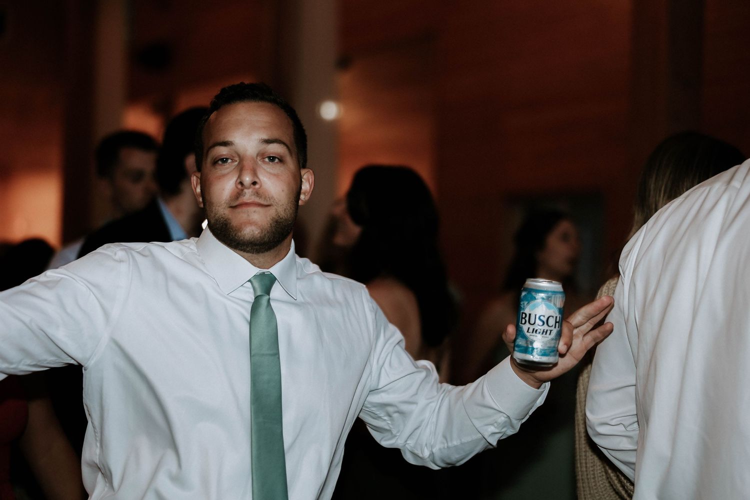 Man in white shirt and green tie holds a Coors Light can at a wedding reception party.