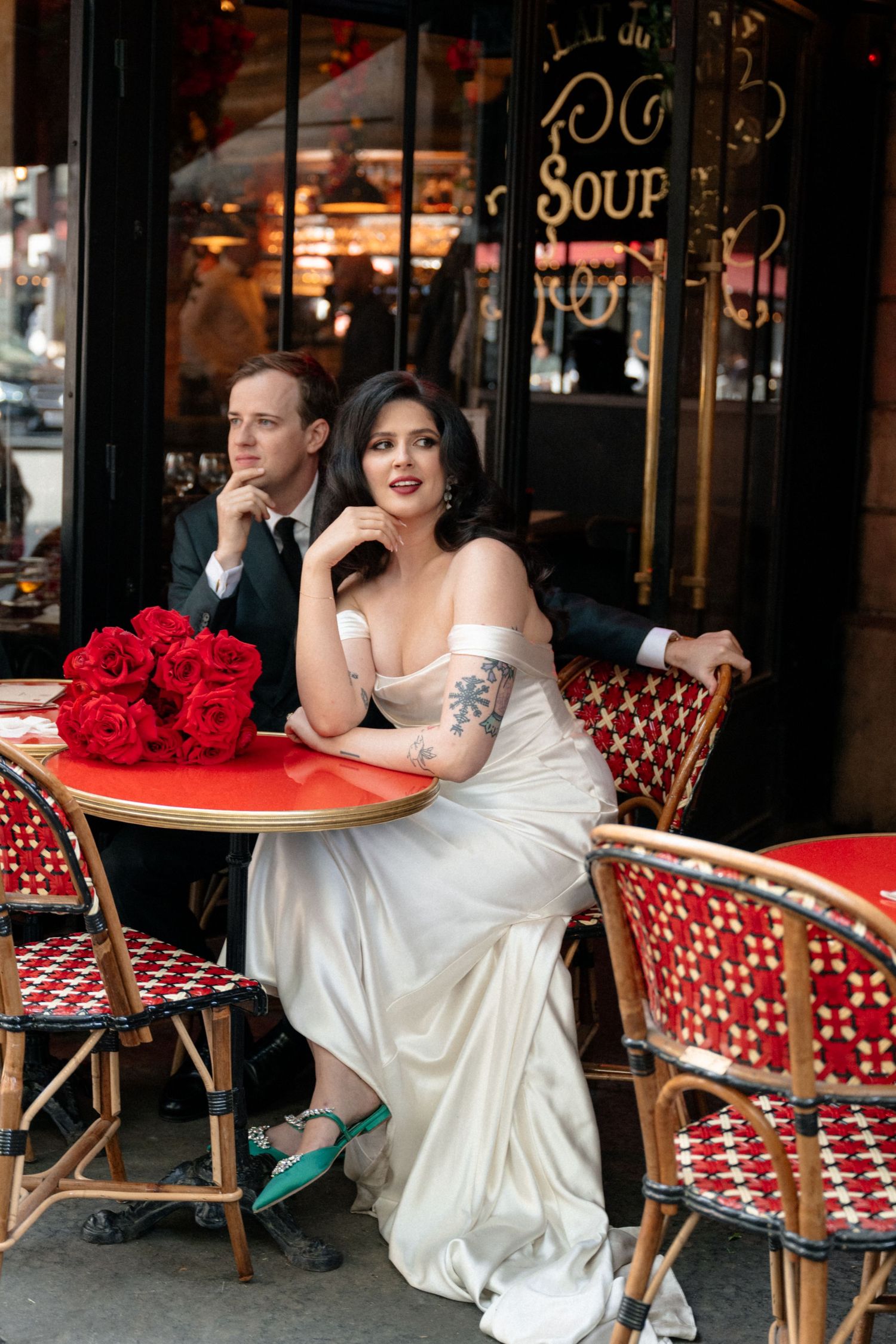 A couple relaxes at a Parisian-style cafe with red chairs and outdoor seating.