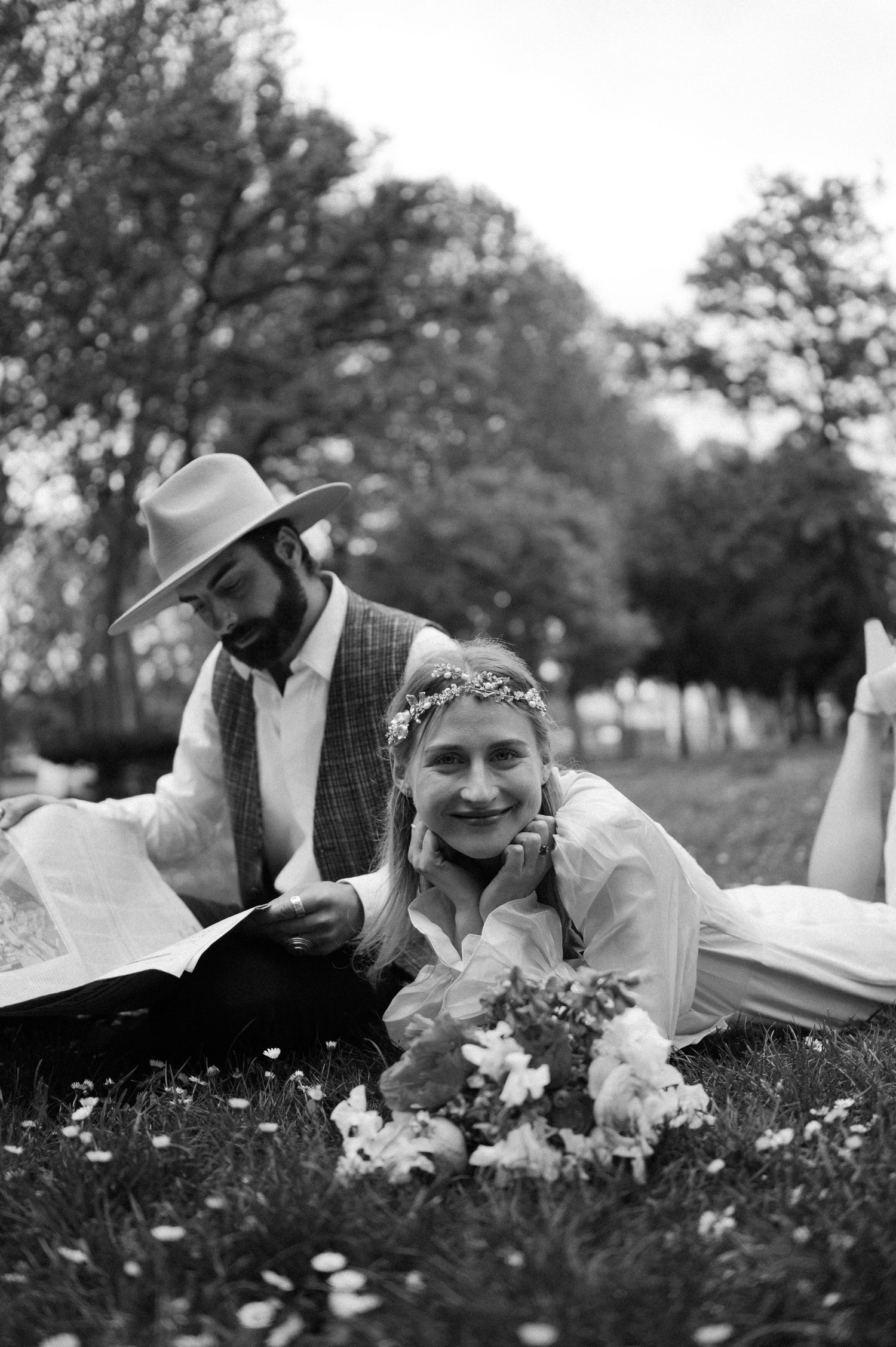 Black and white image of couple reading together on flower-dotted lawn.
