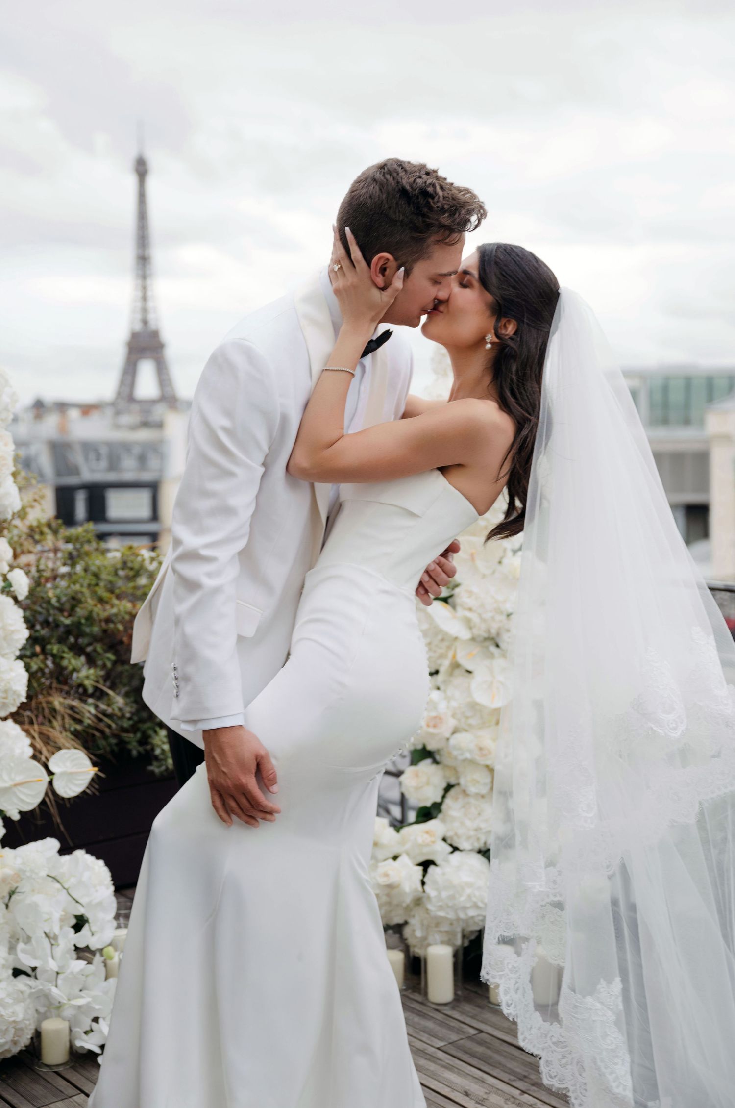 Bride and groom sharing a romantic kiss on a Parisian rooftop with the Eiffel Tower in the background.