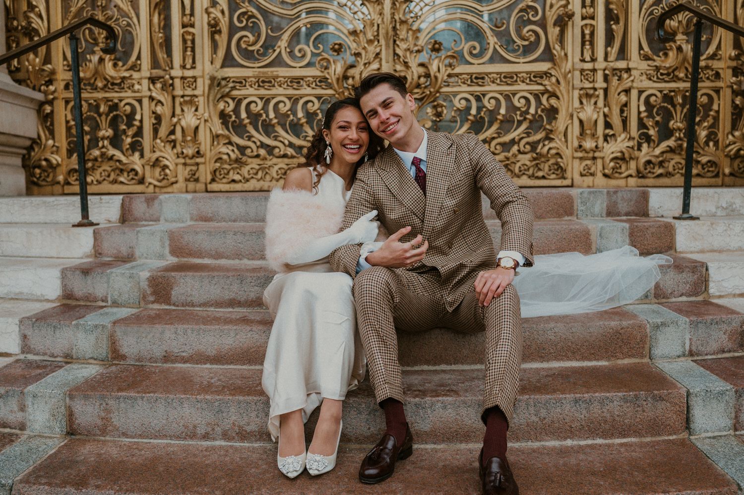 Couple in vintage wedding attire share intimate moment on stone steps.