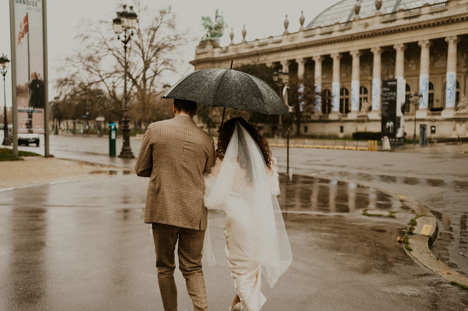 Romantic couple walking in the rain with umbrella near historic colonnade building.