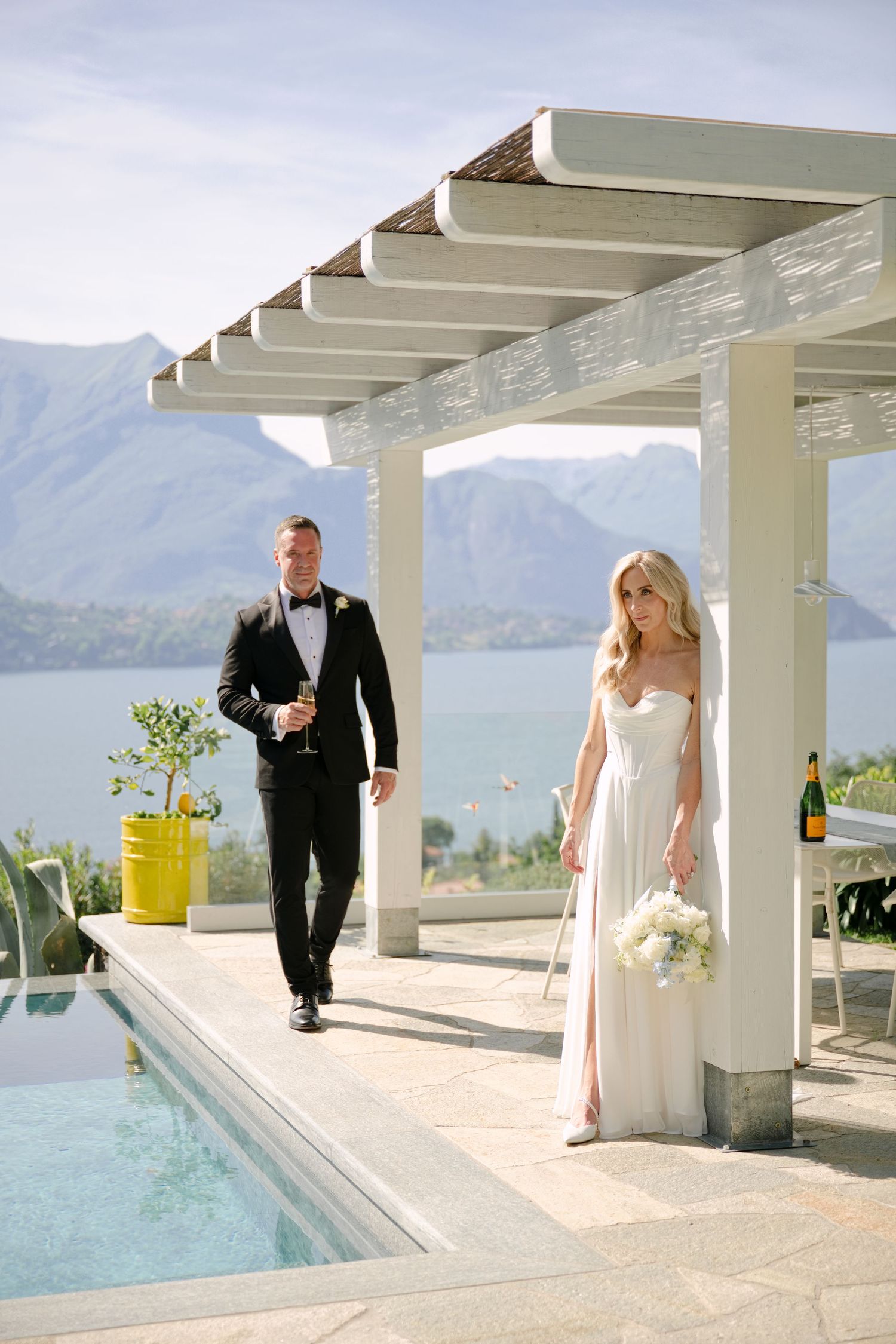 Bride and groom walking poolside at luxury villa with stunning mountain lake views on their wedding day.